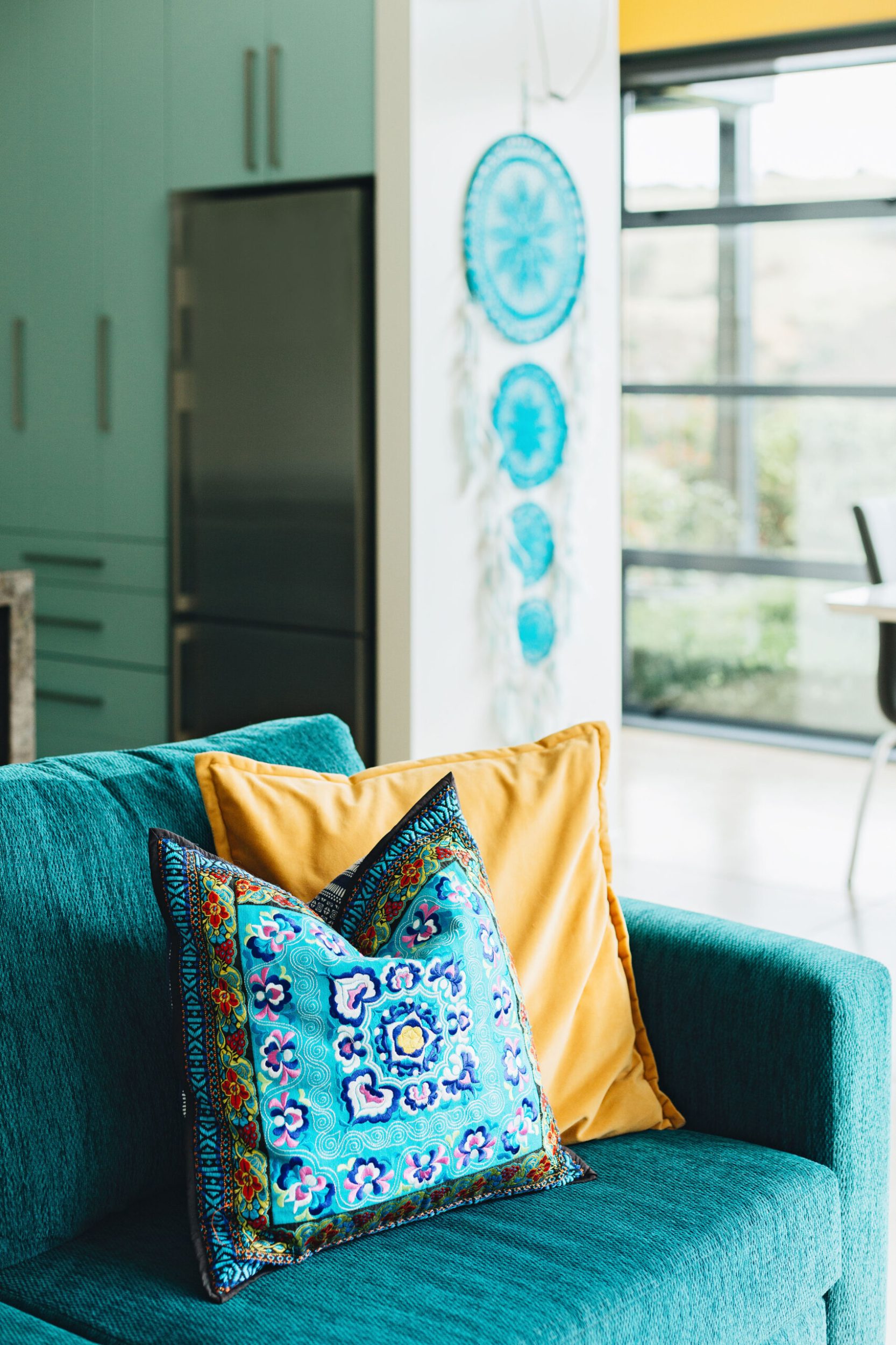 An emerald green velvet couch with blue and yellow boho cushions