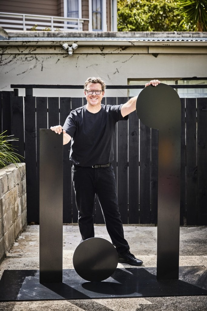 David Alsop standing in courtyard by black art sculptures 
