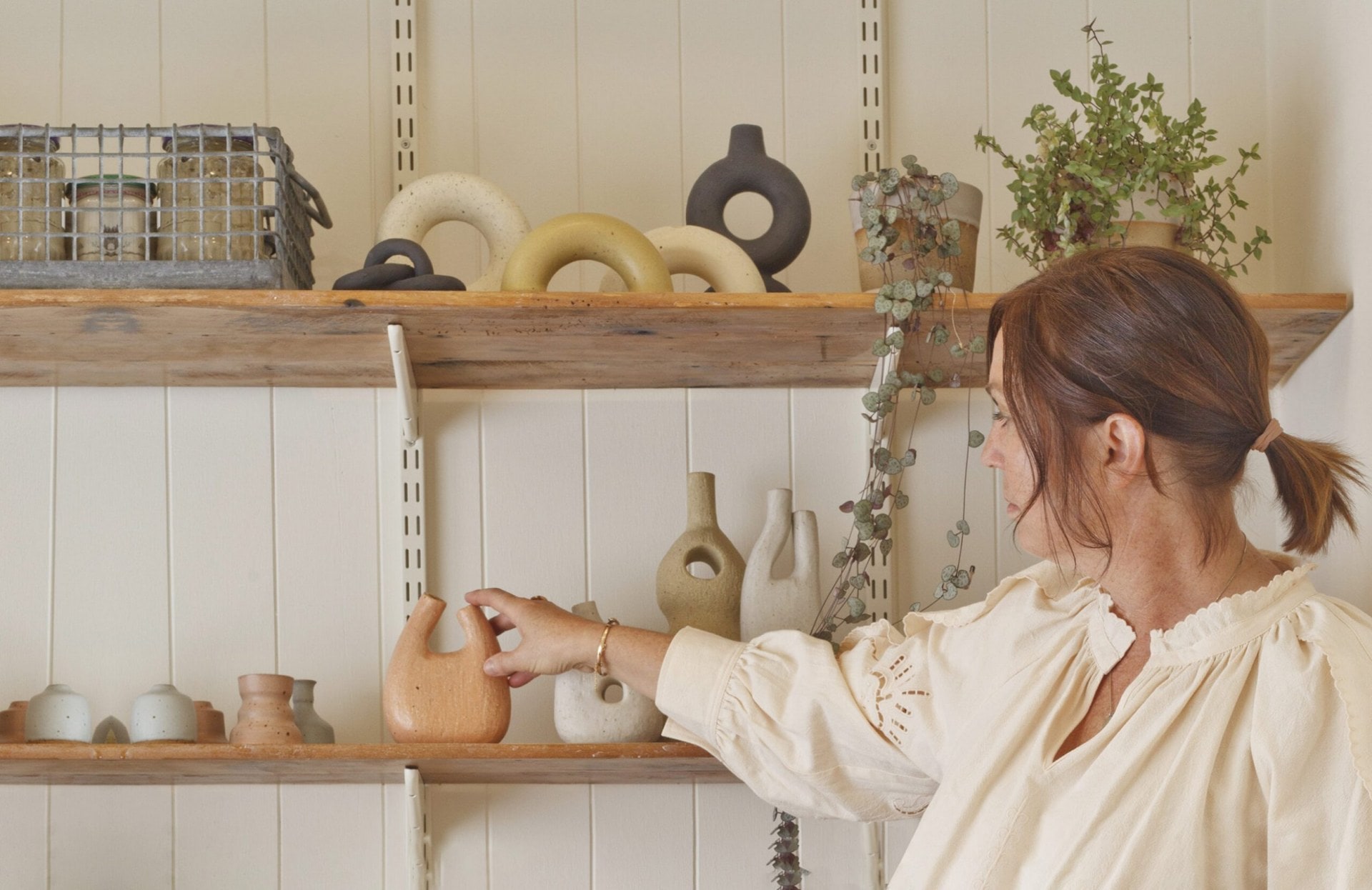 Deborah Sweeney reaching out to touch a ceramic ornament on a shelf filled with assorted ceramics