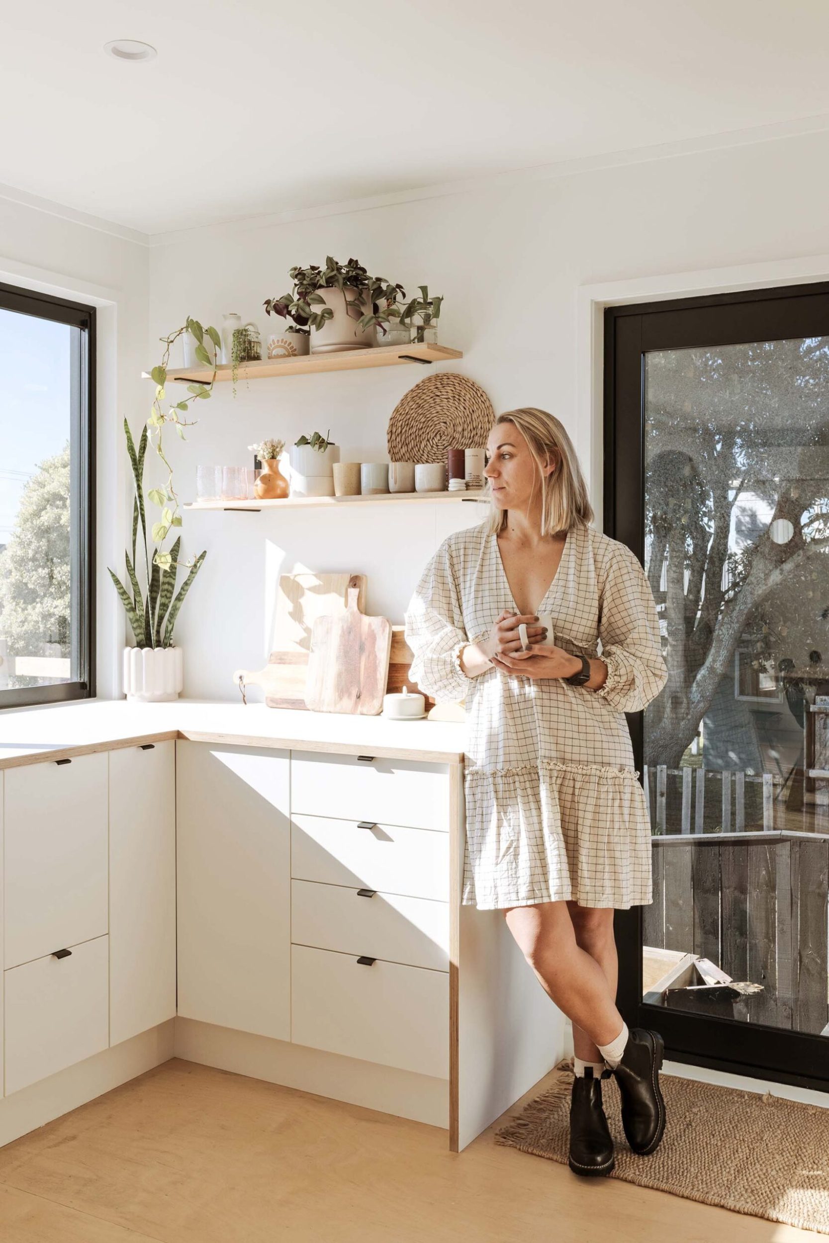 Debbra Sweetman leaning against a white kitchen cabinet holding a cup of coffee