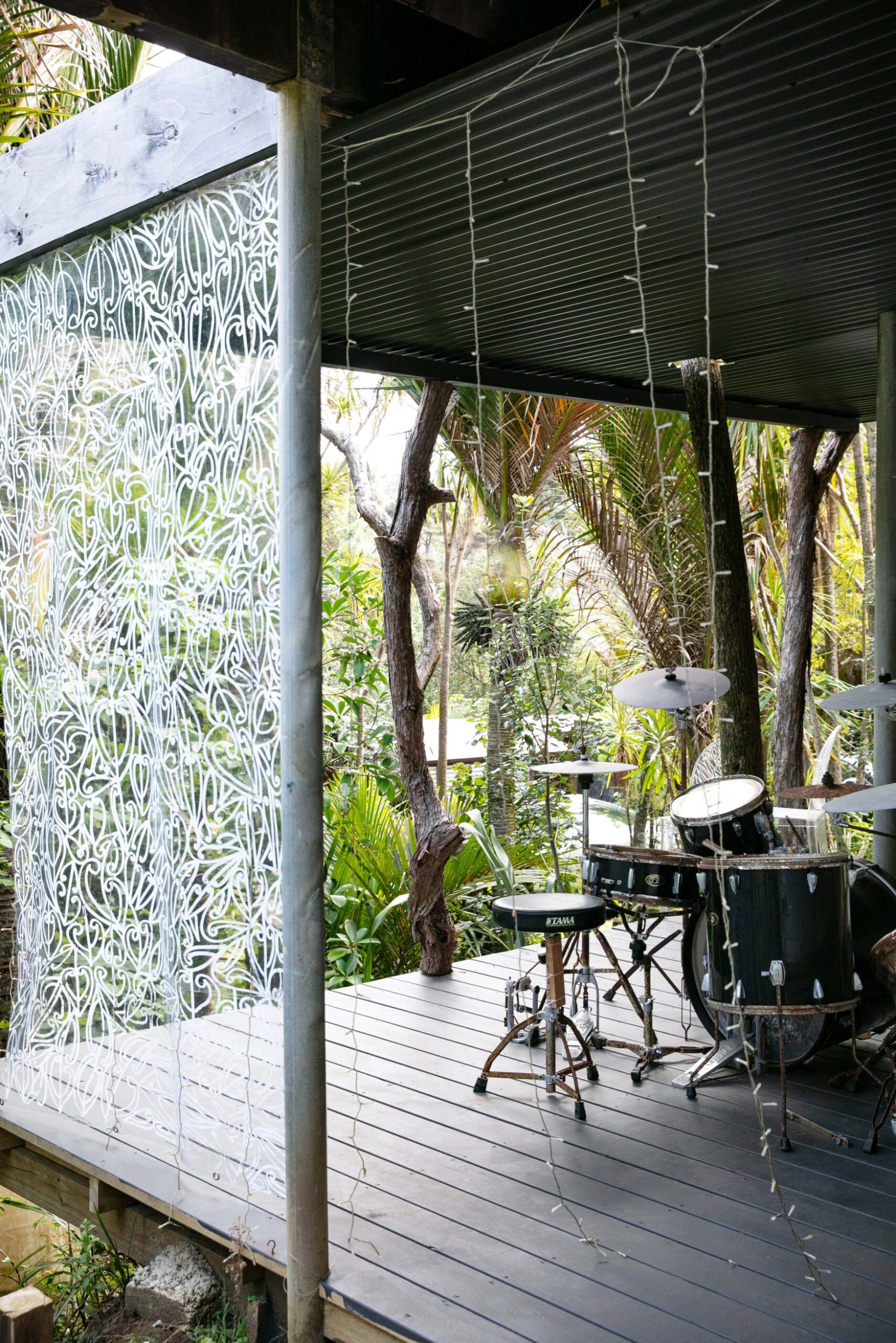 An open plan black deck in bush, a drum set and hanging fairy lights