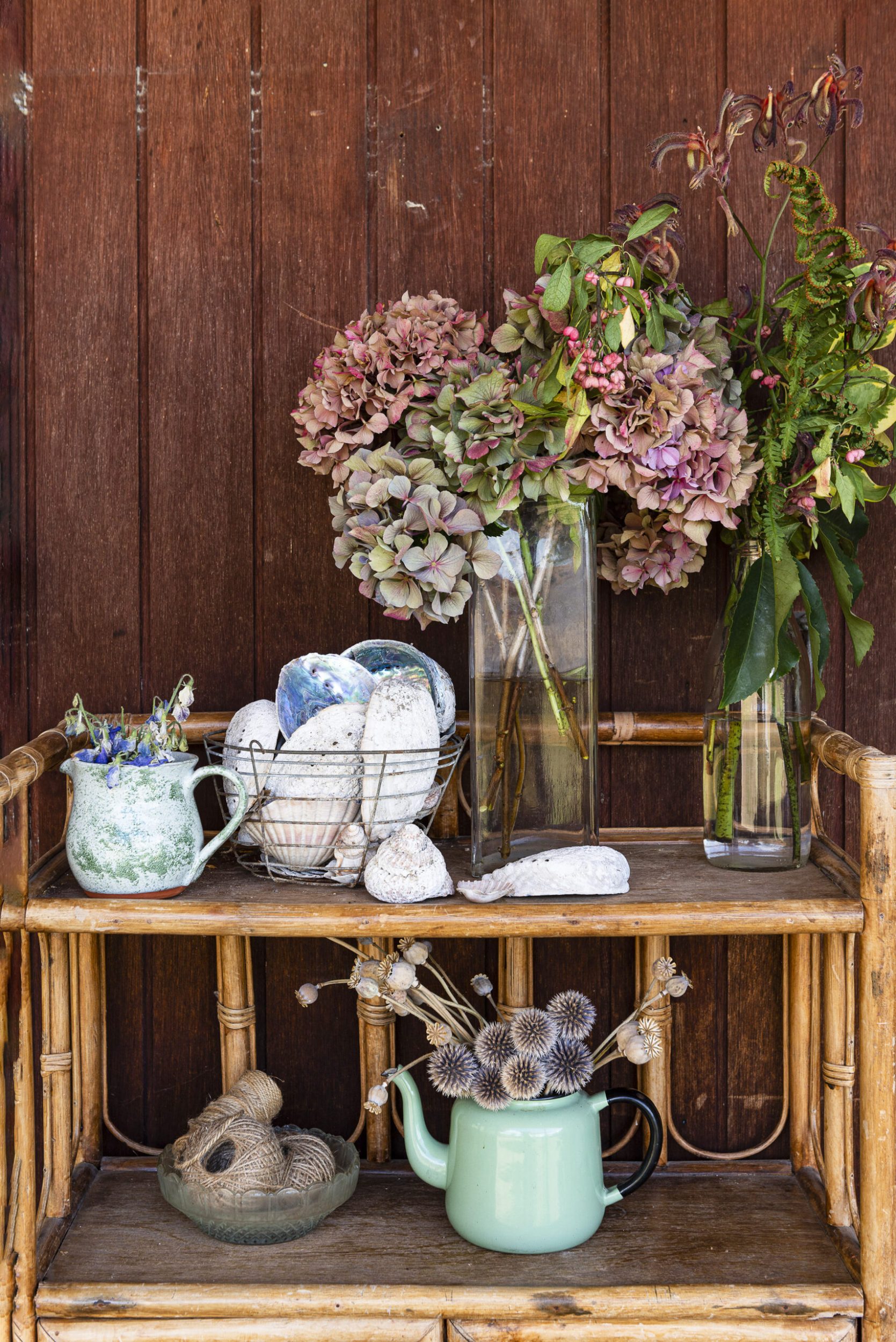 Vintage brown brown shelf unit with assorted vases with flowers, blue tea cups and sea shells