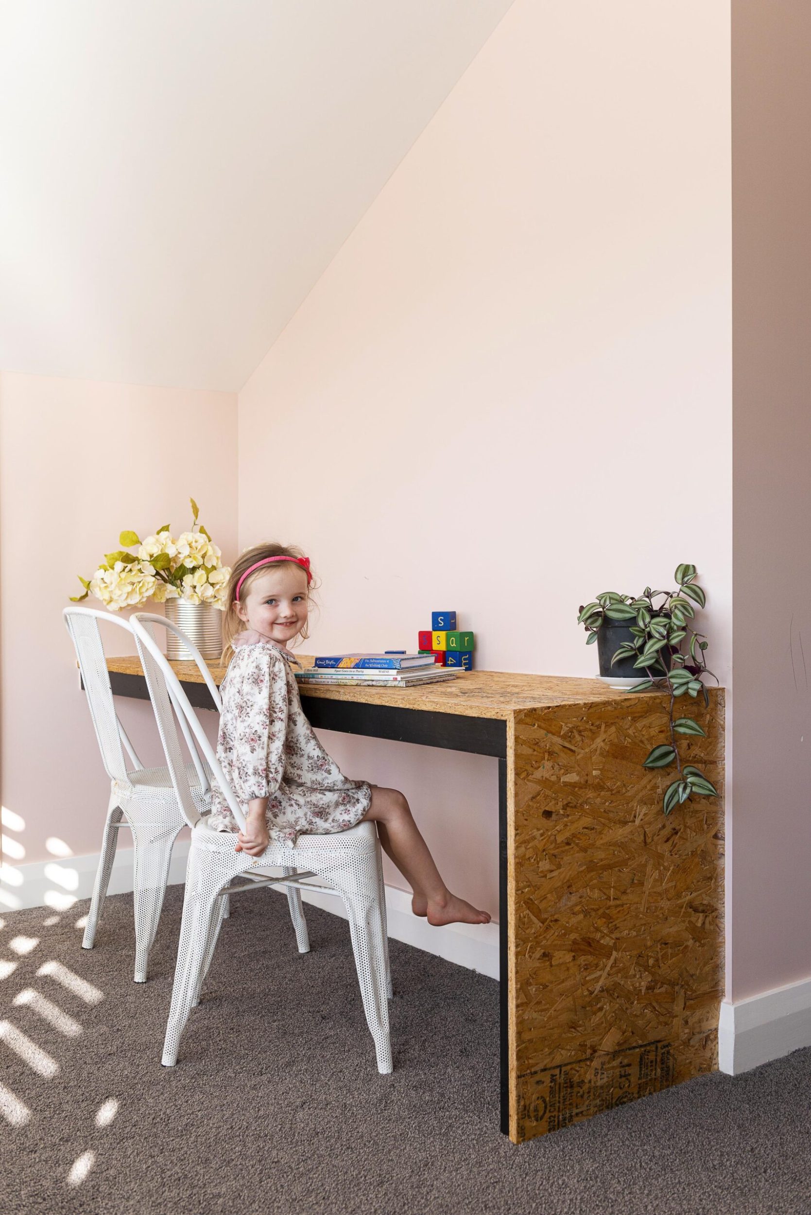 A little girl sitting in a pink room with a rustic inbuilt wooden desk 
