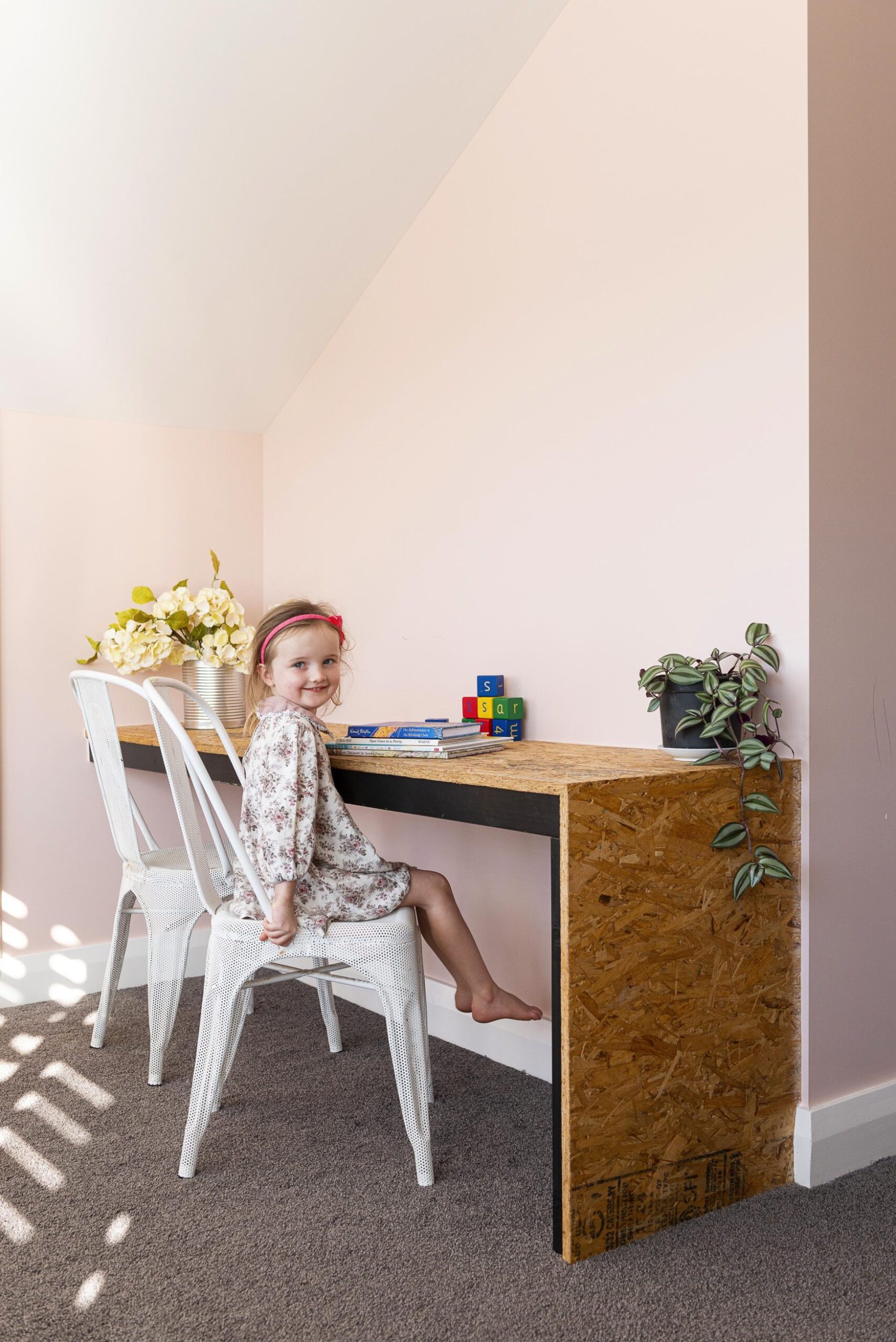 A little girl sitting in a pink room with a rustic inbuilt wooden desk