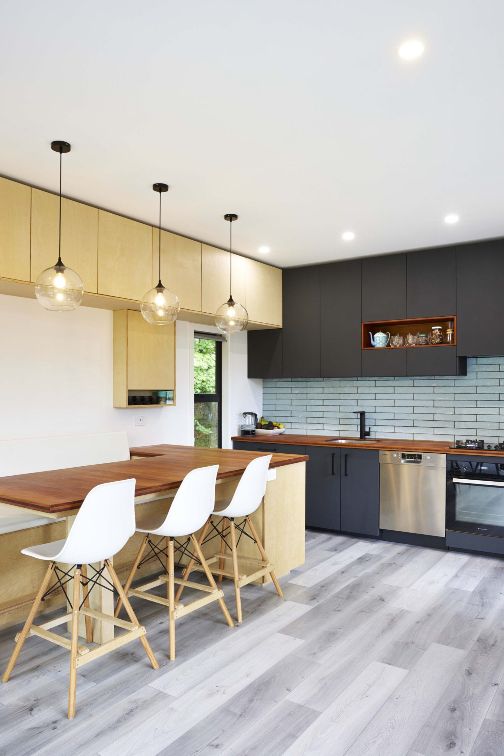 A black kitchen and dining space with wood panels and hanging pendant lights 