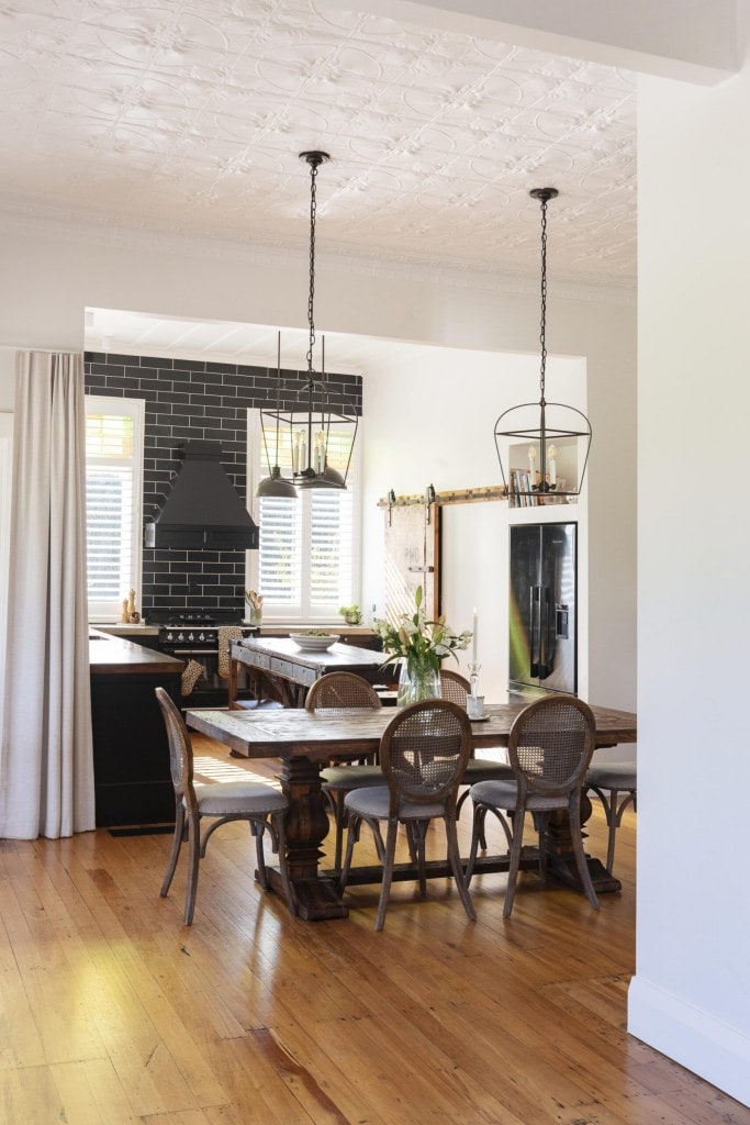 A kitchen and dining room with black subway tiles and a dark wood vintage dining table