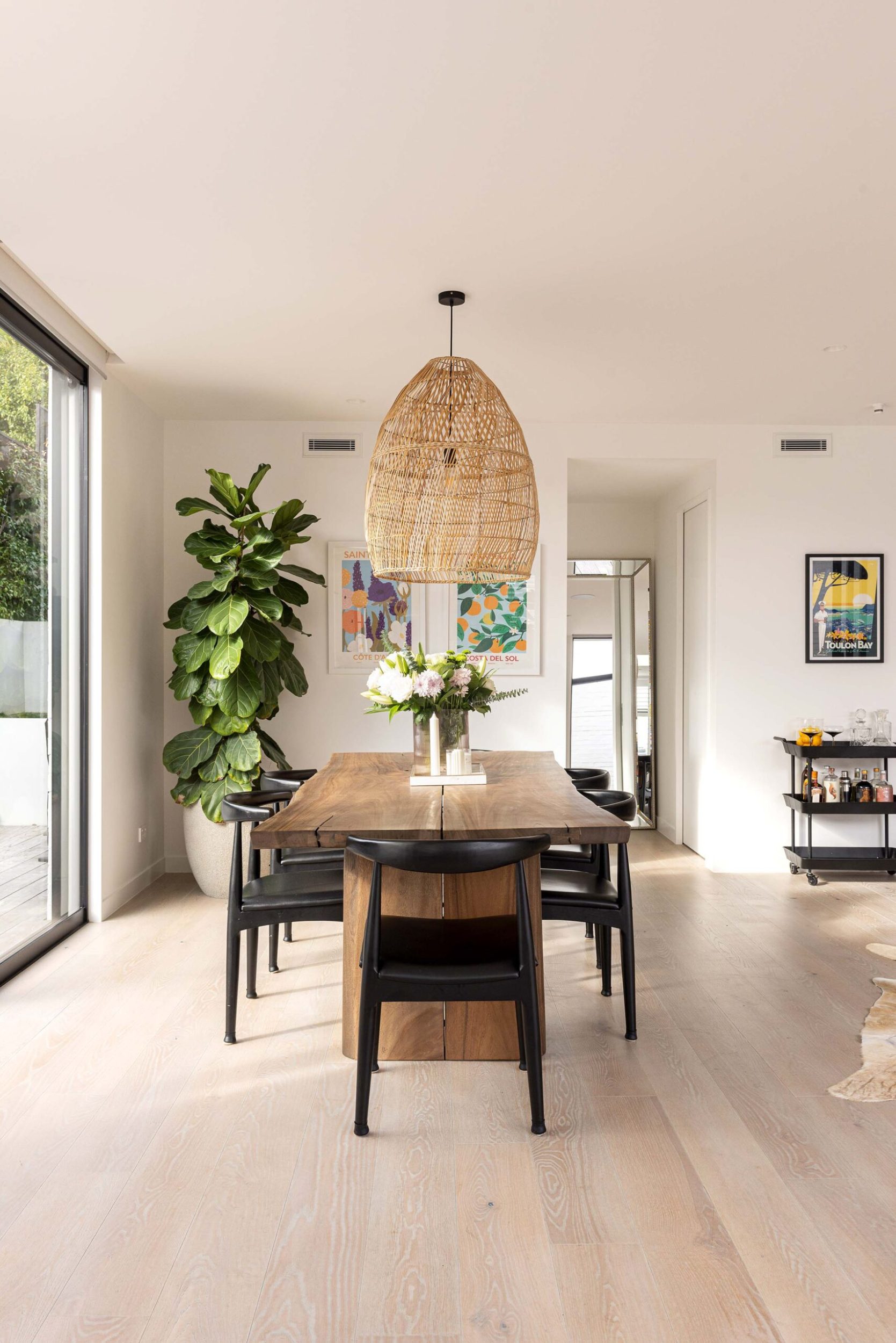 The dining room with a large wicker light shade above a deep timber table with black