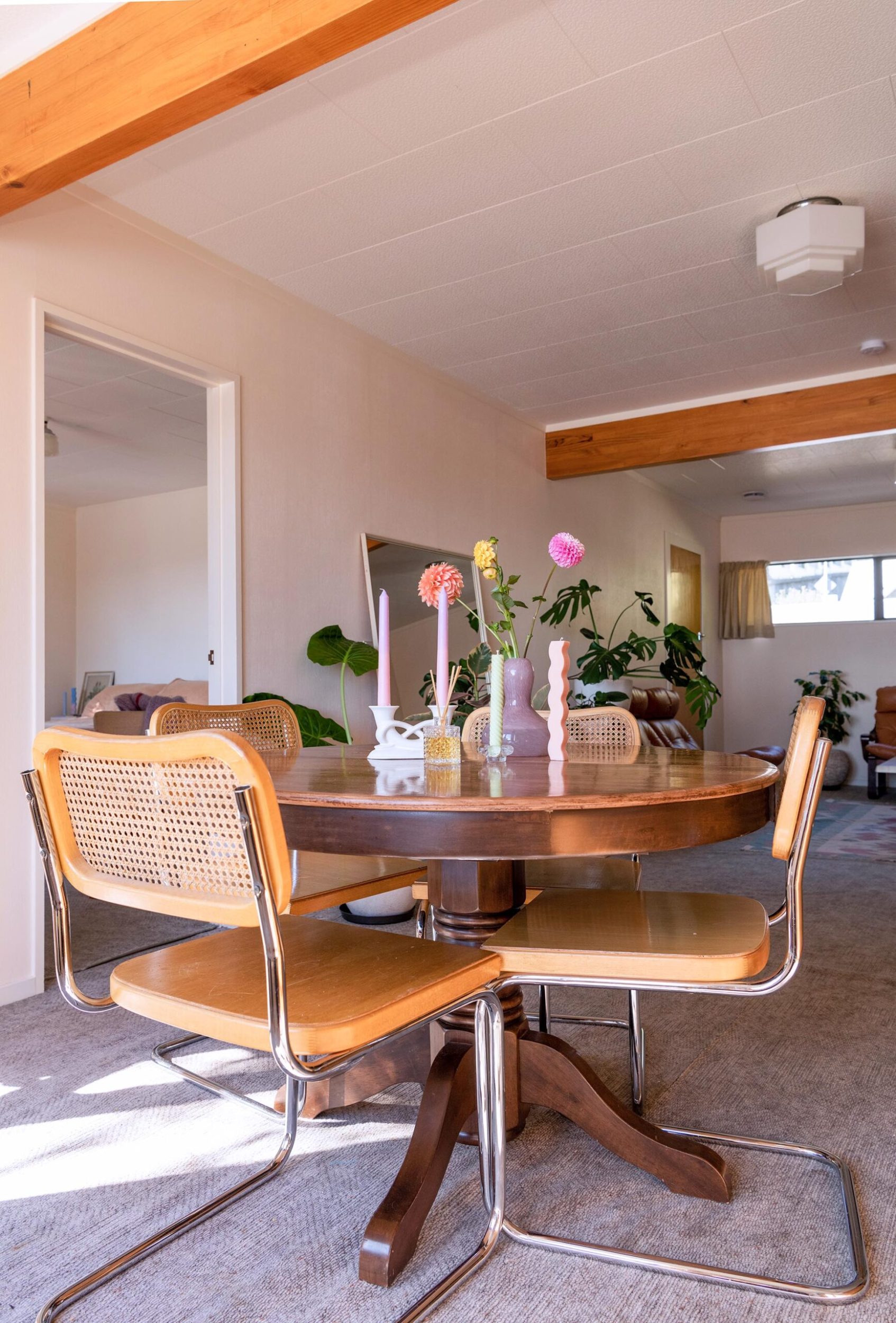 A dining room with a round wood table and matching chairs with multicoloured candles and flowers on top