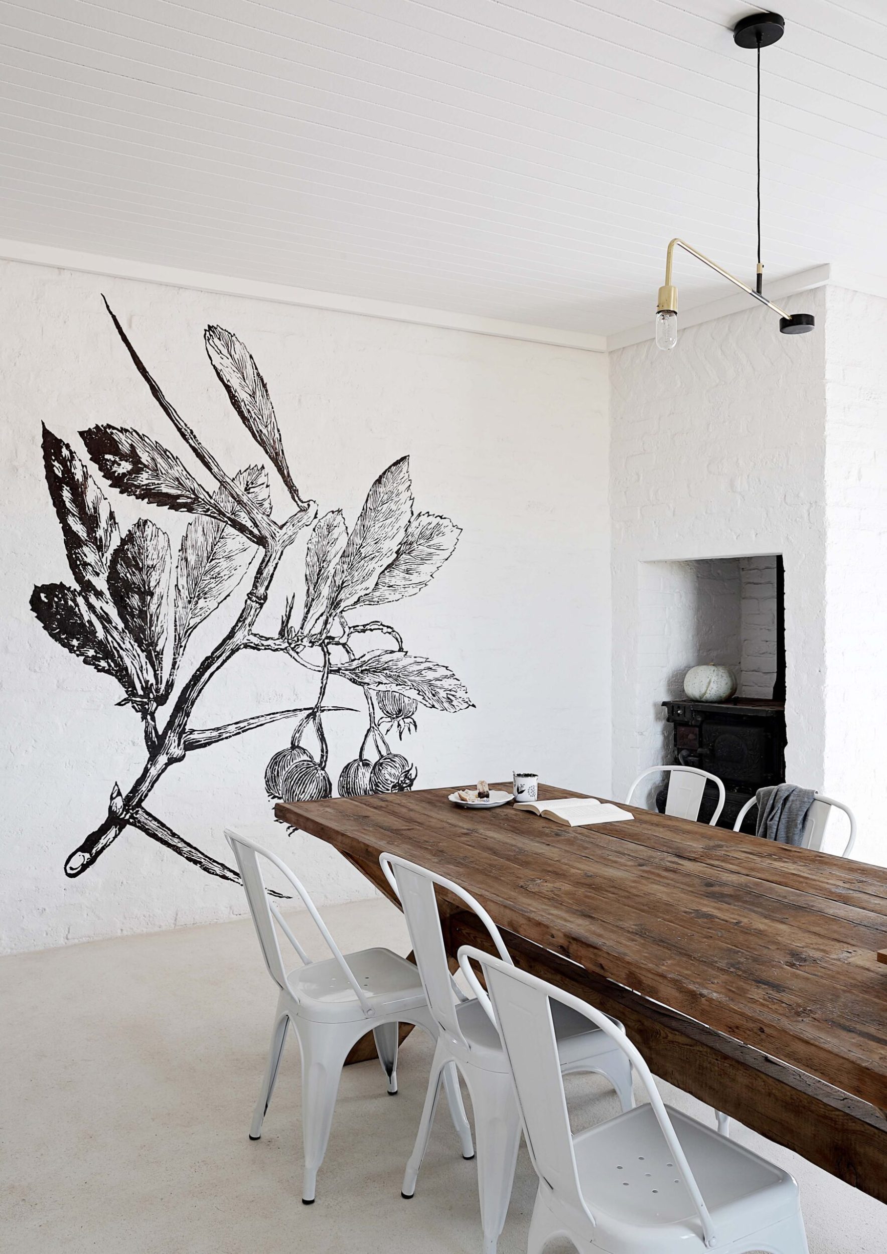 A dining room with white walls and a painted black and white mural of a tree branch