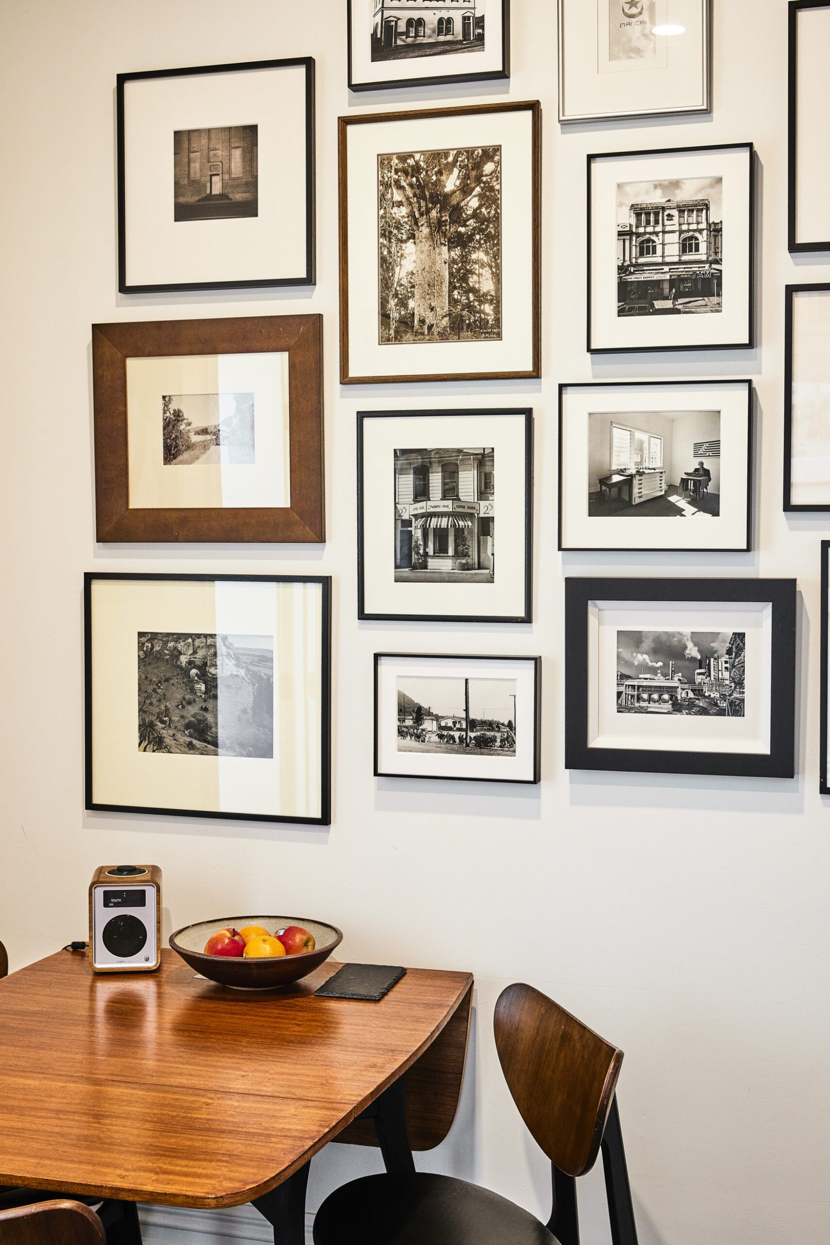 White room with small brown dining table with assorted framed black and white photographs hanging above it