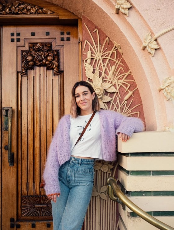 Danni Duncan leaning against pink arched doorway wearing blue jeans and lavender cardigan