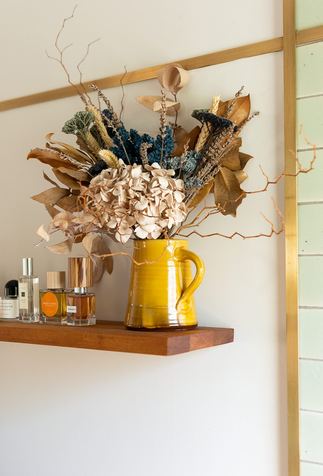 Mustard yellow vase containing dried flowers on brown shelf