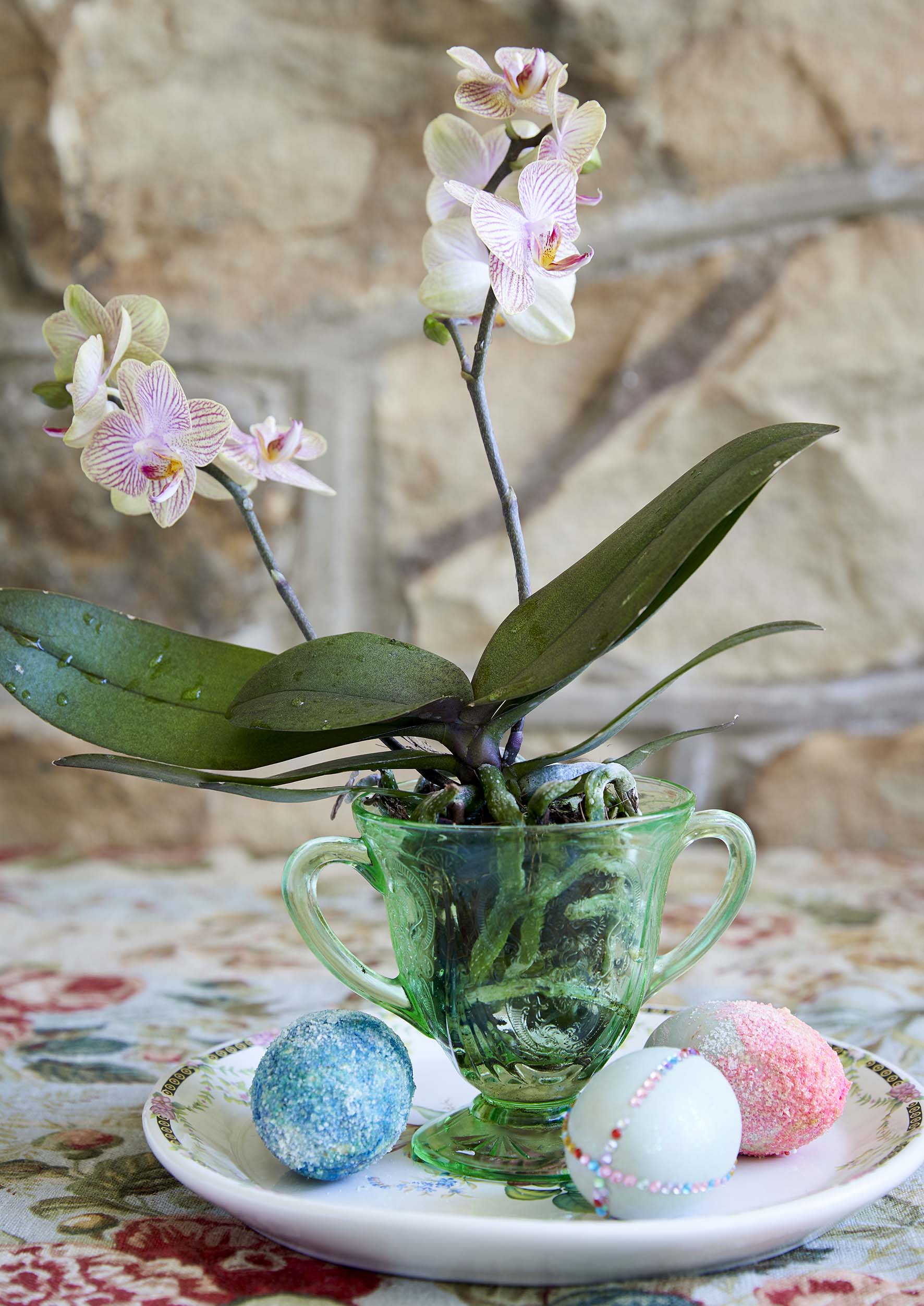 A green round teacup on a round plate with a pink flower plant and assorted coloured Easter eggs