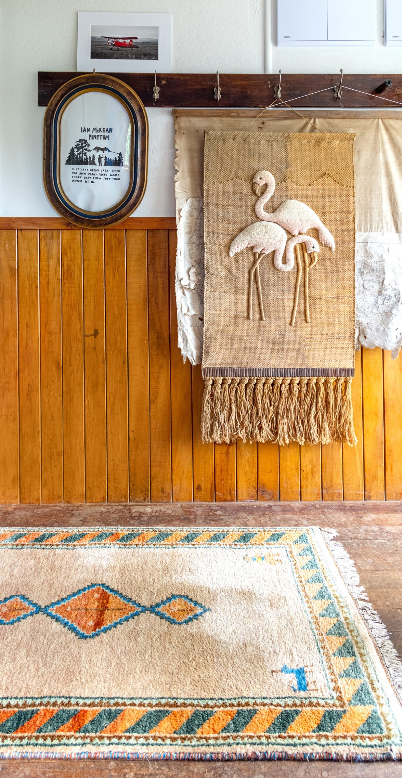 Wall with brown hanging hooks, flamingo decorated tepestry, wood panels and a floor covered by white patterned rug