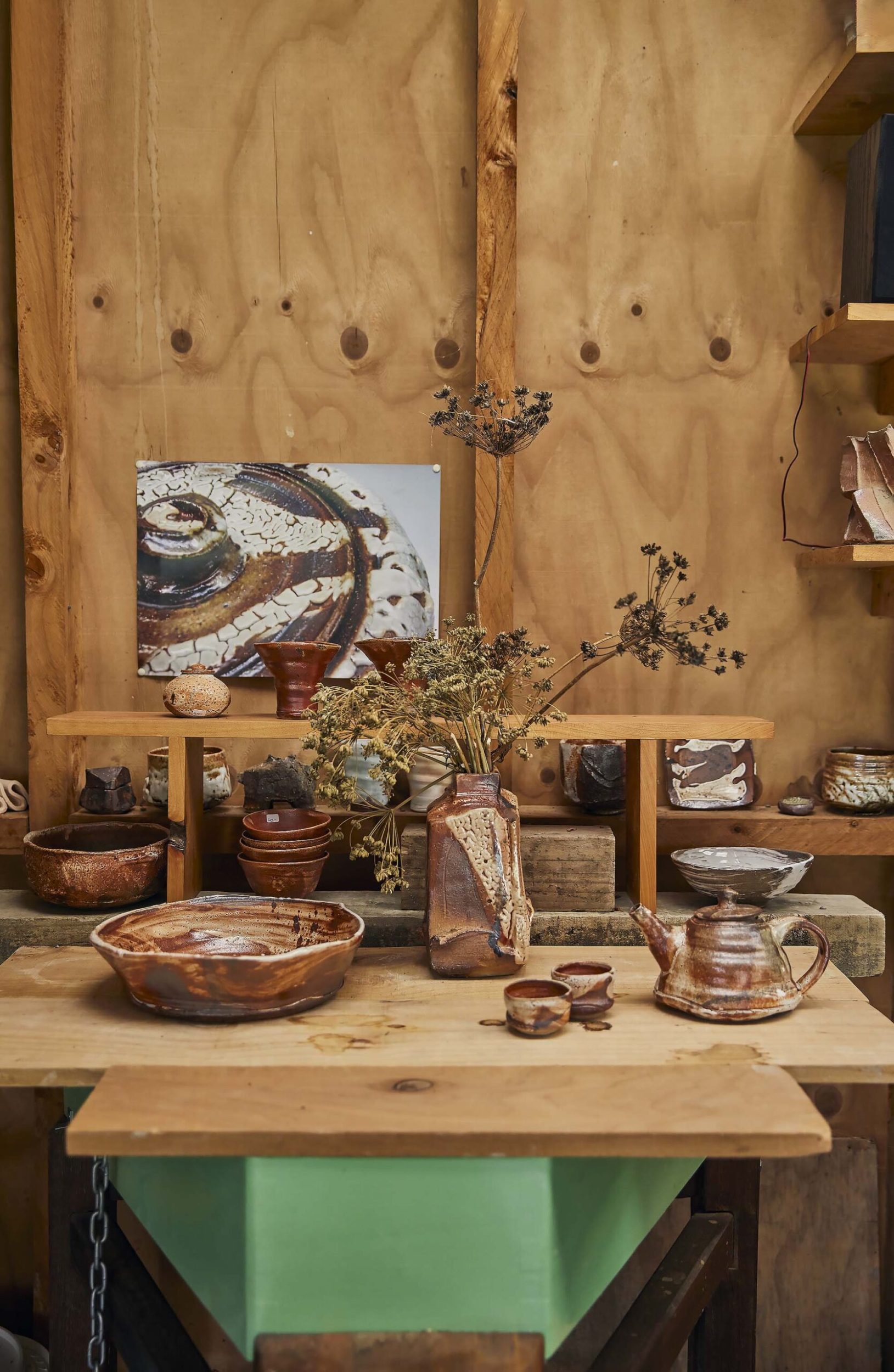 A brown wood table set against a wood wall with Elena Renker ceramics and art set on it