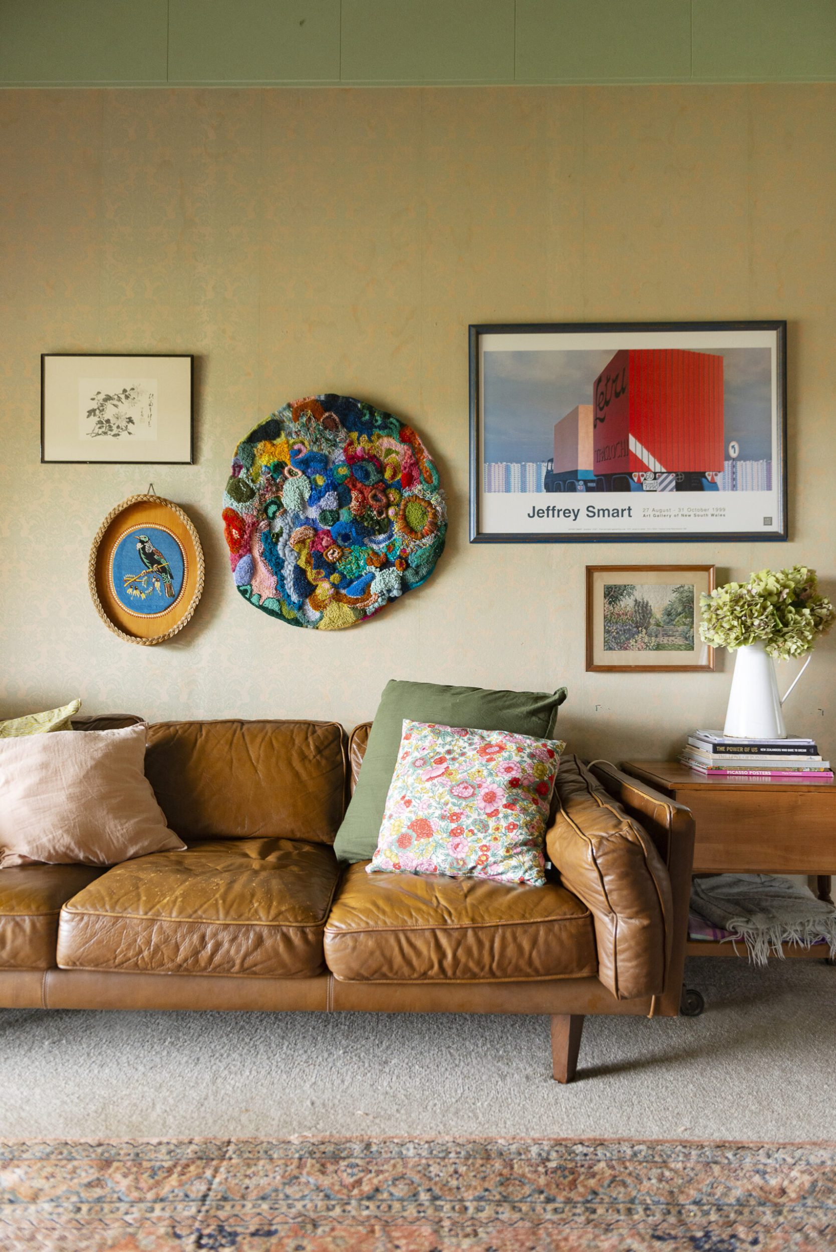 Brown couch in green room with hanging embroidery art by Fleur Woods