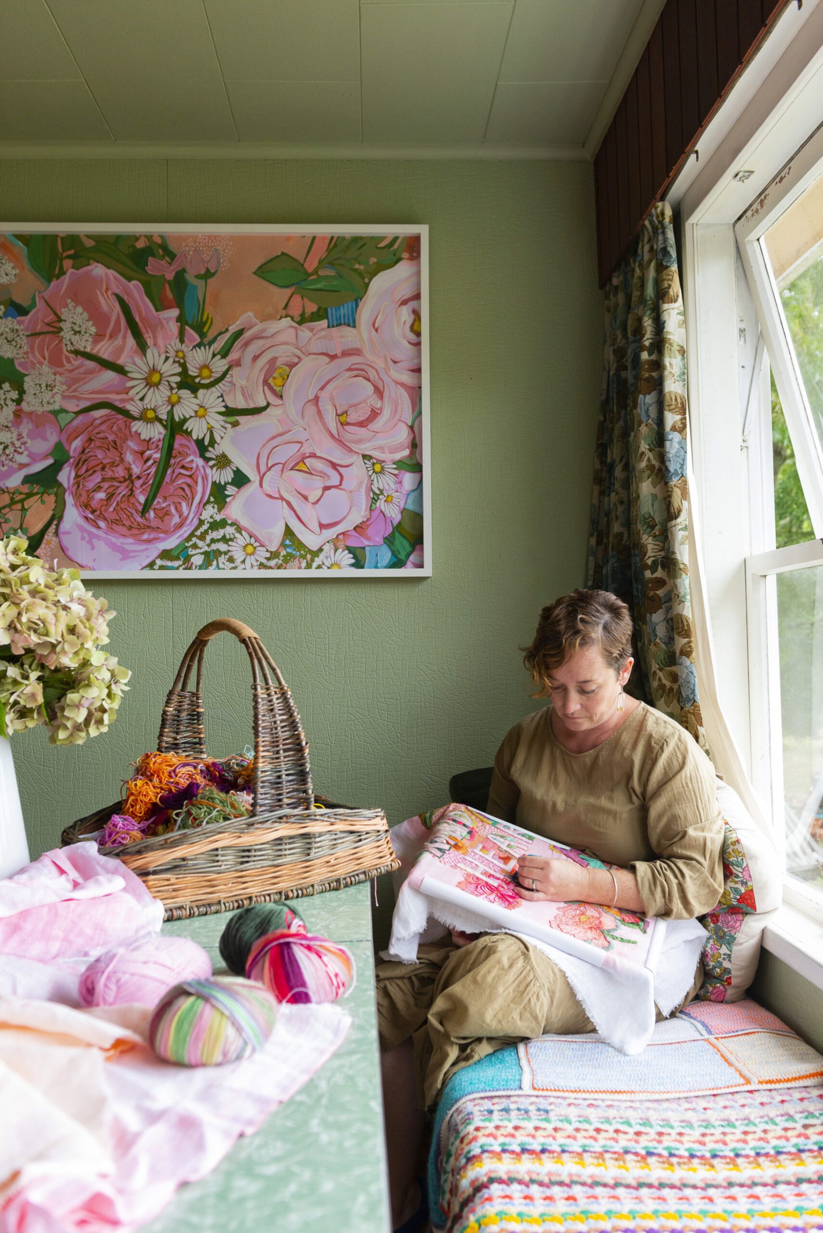 Fleur Woods sitting on colourful couch embroidering white cloth