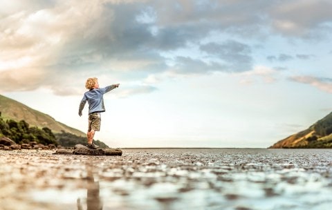 Child pointing up while standing over an estuary