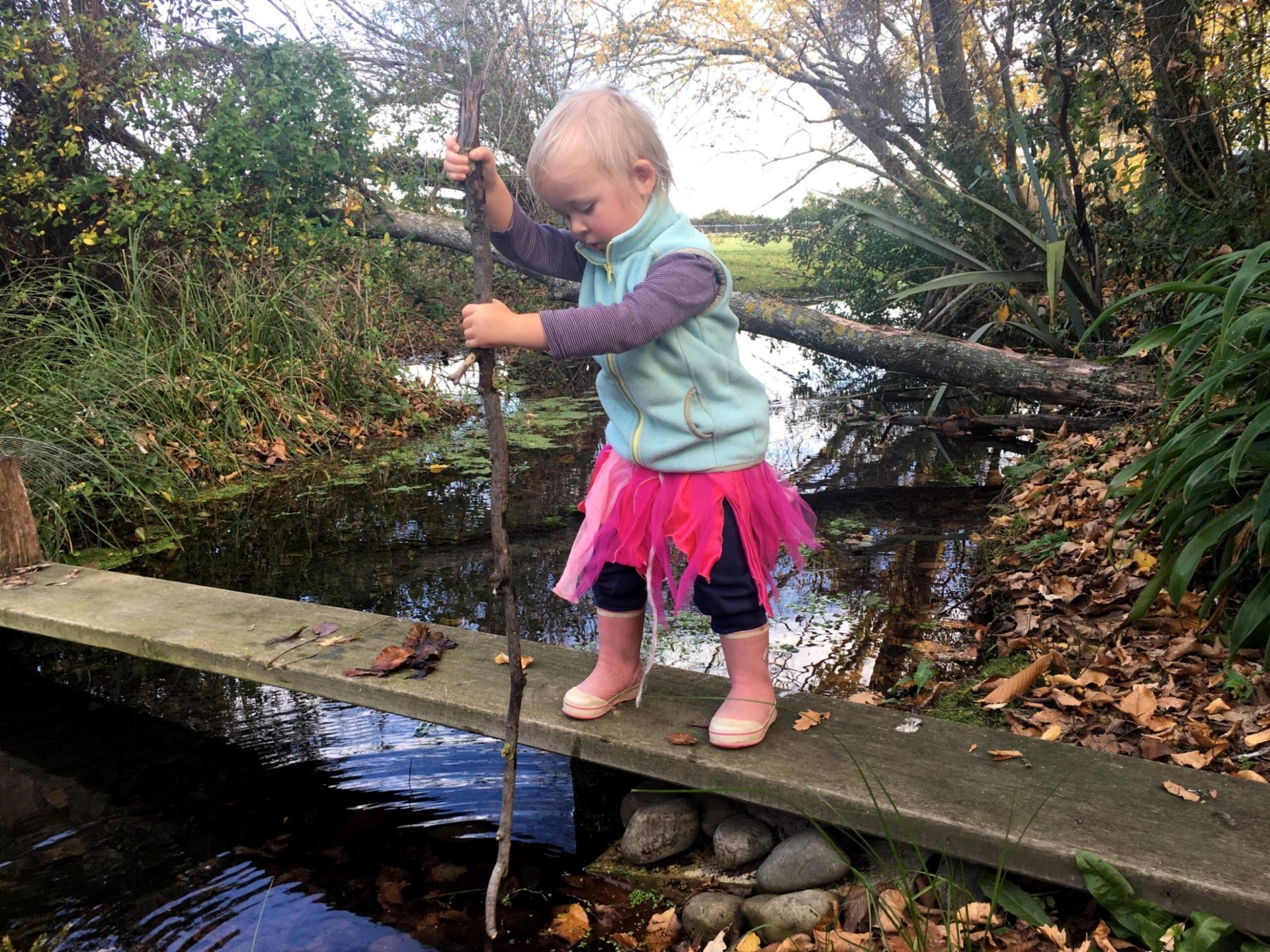 A young girl standing on a makeshift bridge over a stream