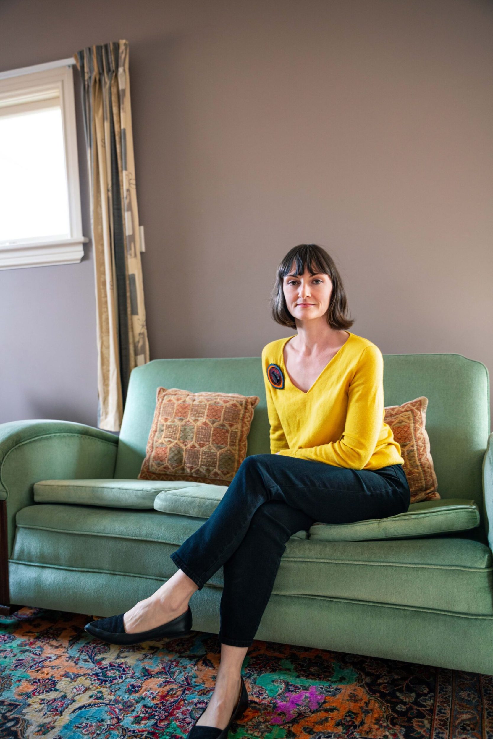 Octavia Cook sitting on a green retro couch wearing a yellow top with a colourful pin