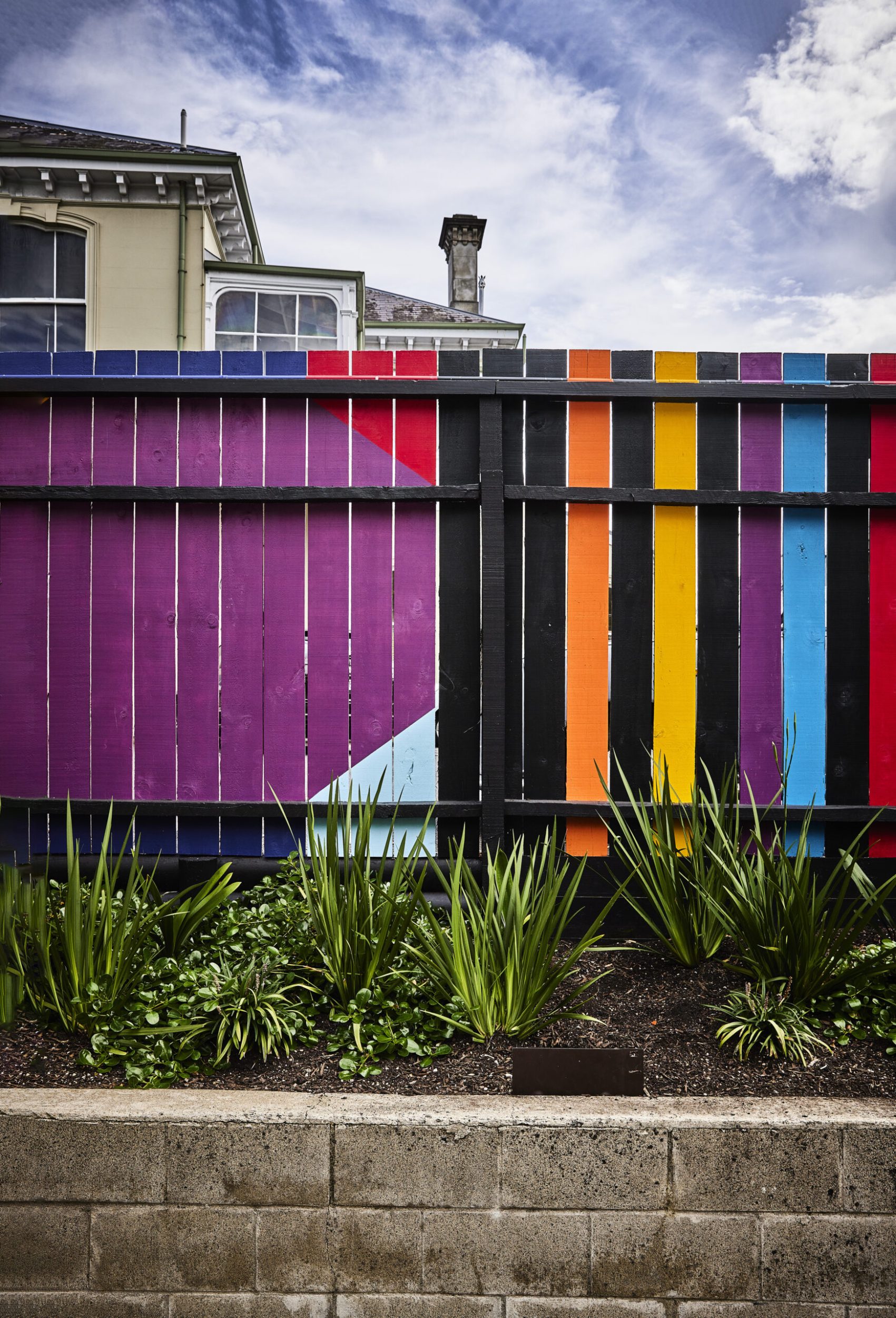 A colourful fence painted black, purple, orange, yellow, red and teal at various angles