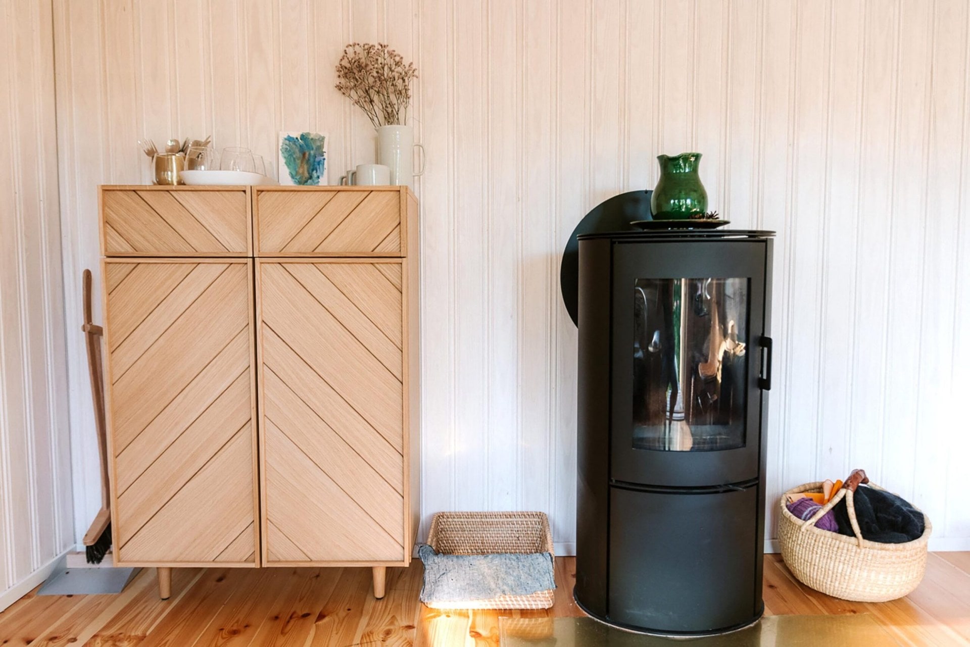 A small round fireplace and geometric patterned small cupboard in a light wood panelled room