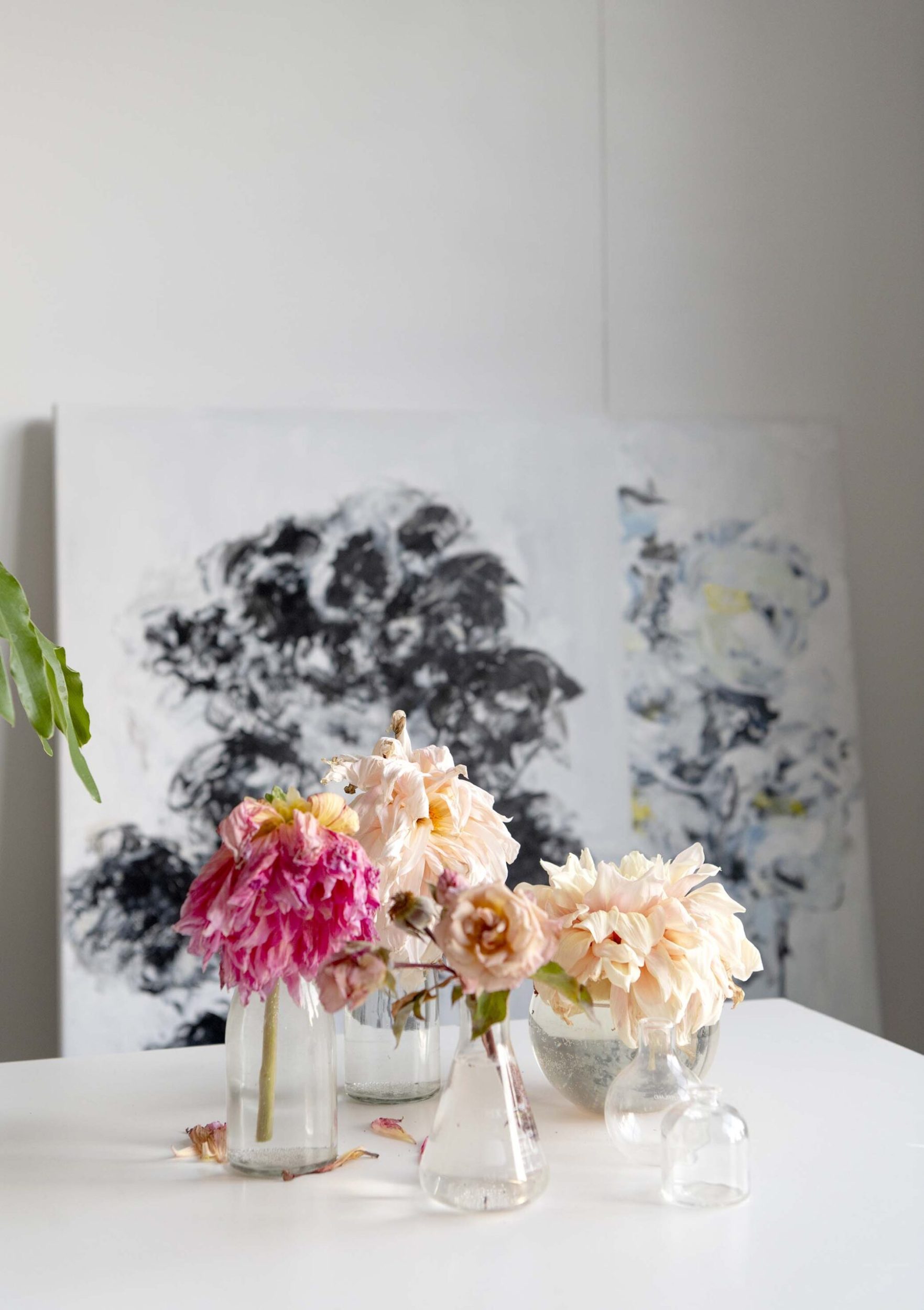 Glass beakers and jars on a white table with various wilting flowers