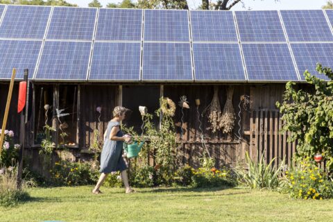 Woman with watering can next to roof of solar panels