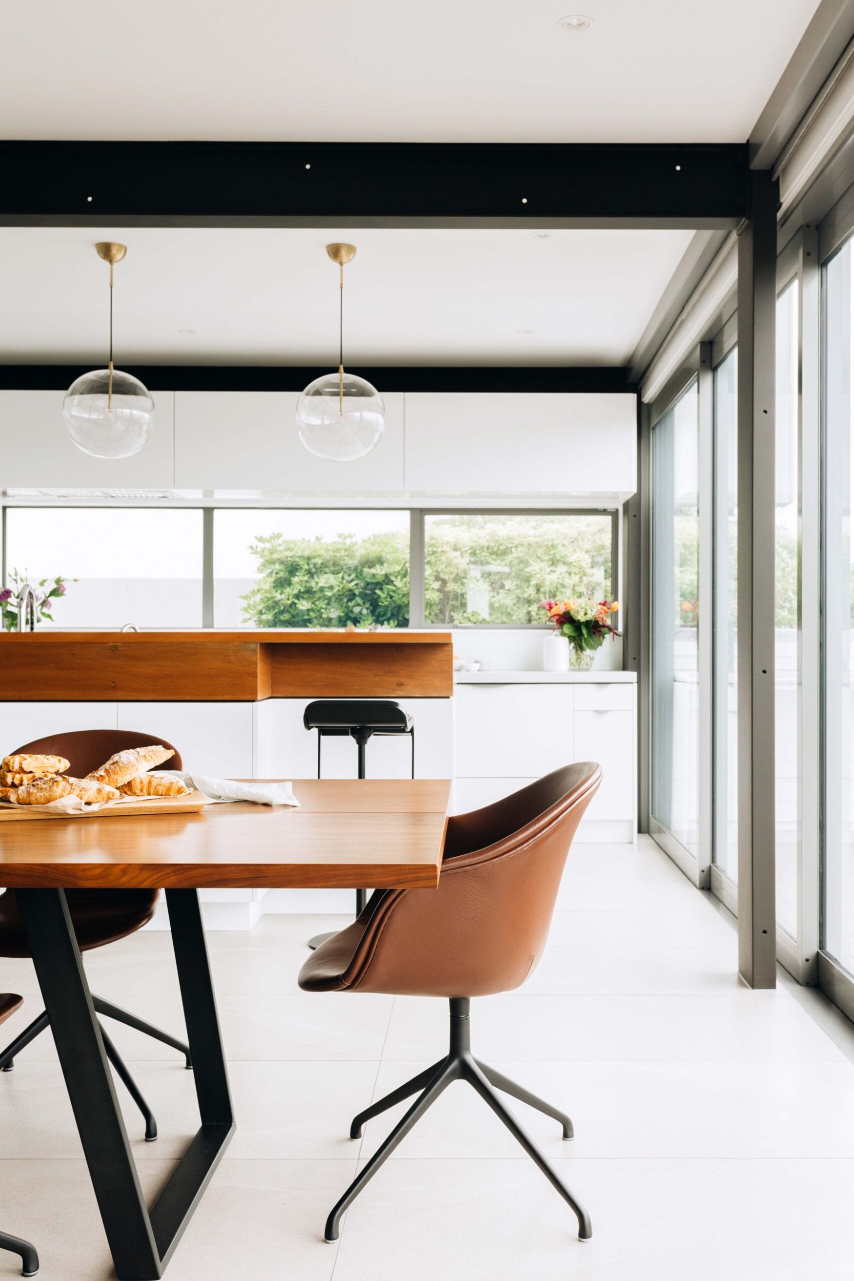 Dining and kitchen room with large glass windows, white drawers and steel black beams on the ceiling 