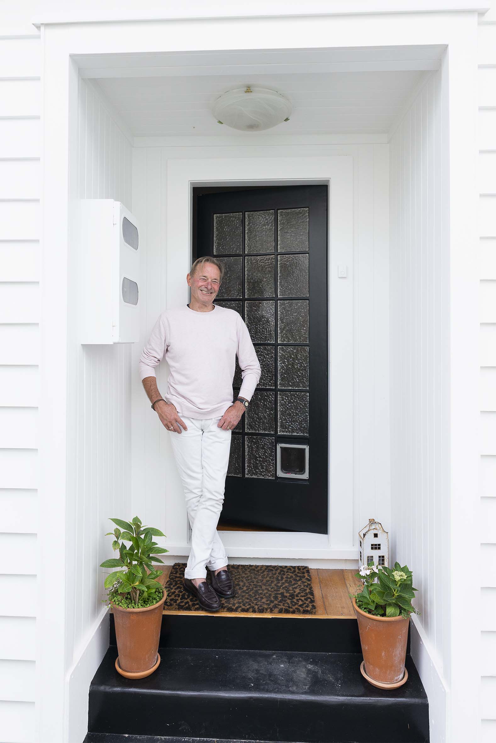 Grant Allen standing by black door wearing white outfit