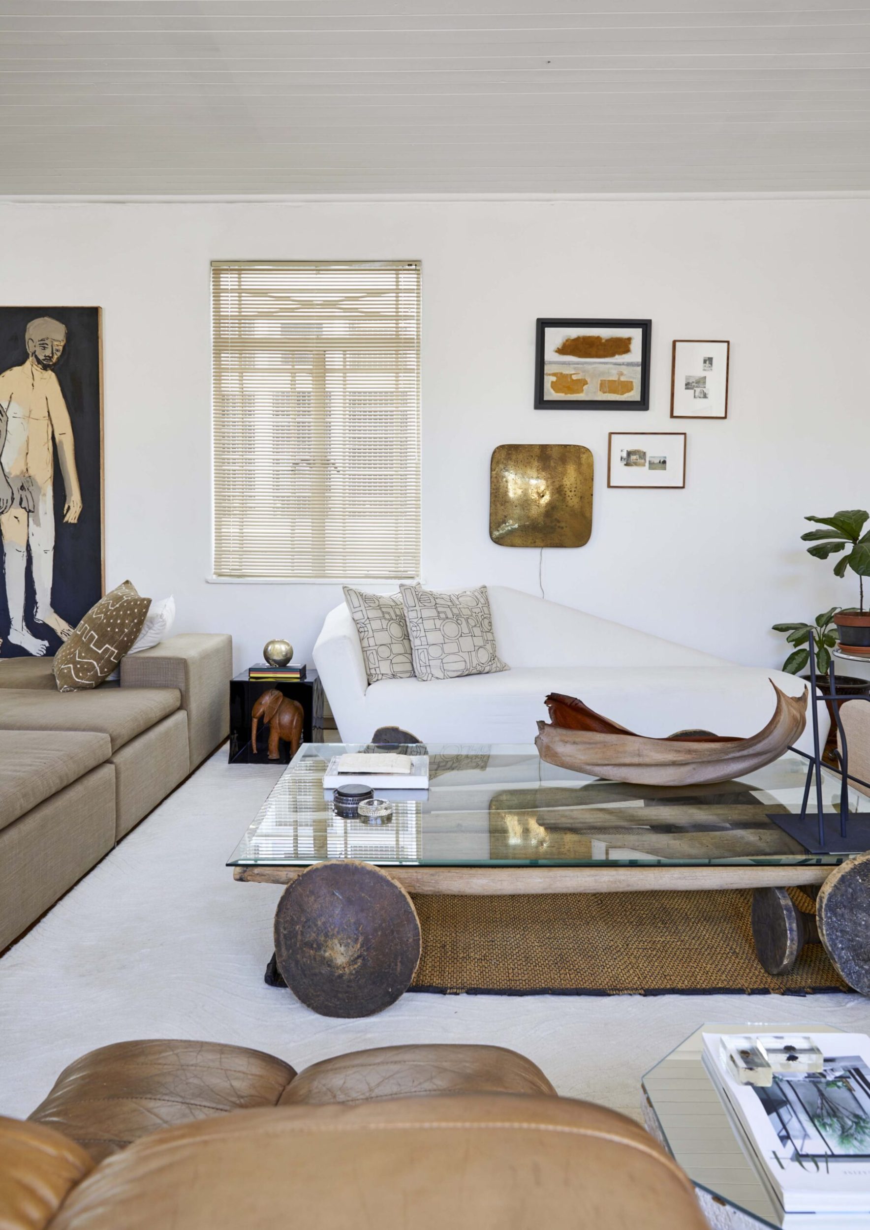 Living room with white walls , a white carpet, brown leather couches and assorted hanging wall art