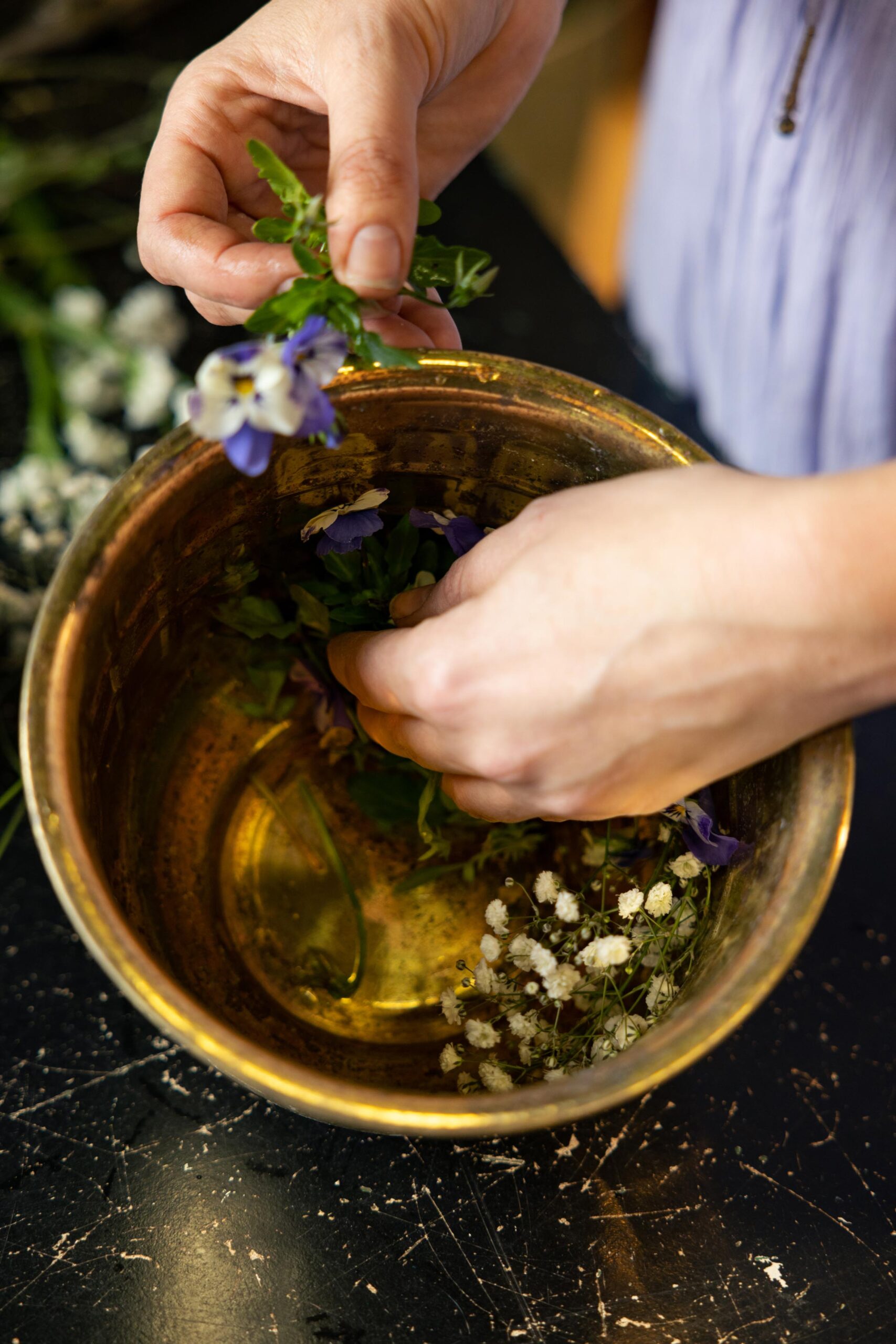 A hand from a person in a purple dress, placing flowers in a ring in a medium sized bowl