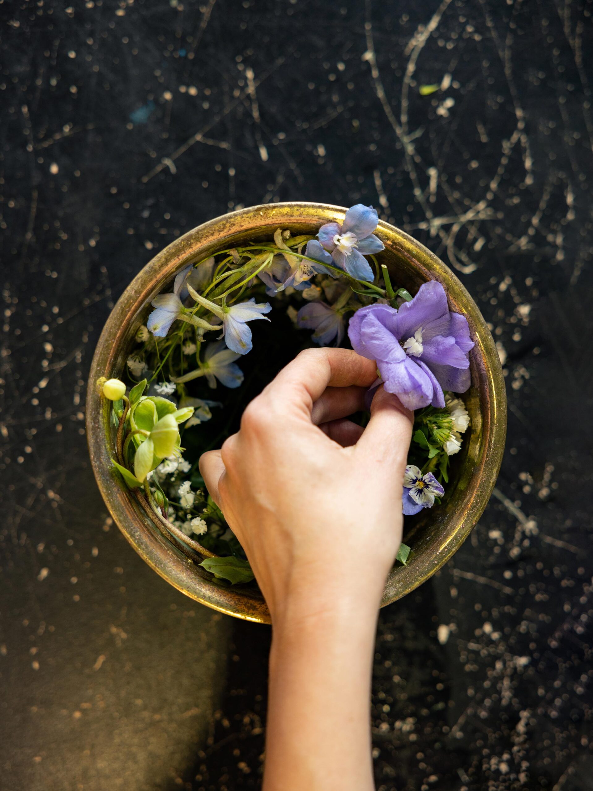A hand placing flowers in a medium sized bowl