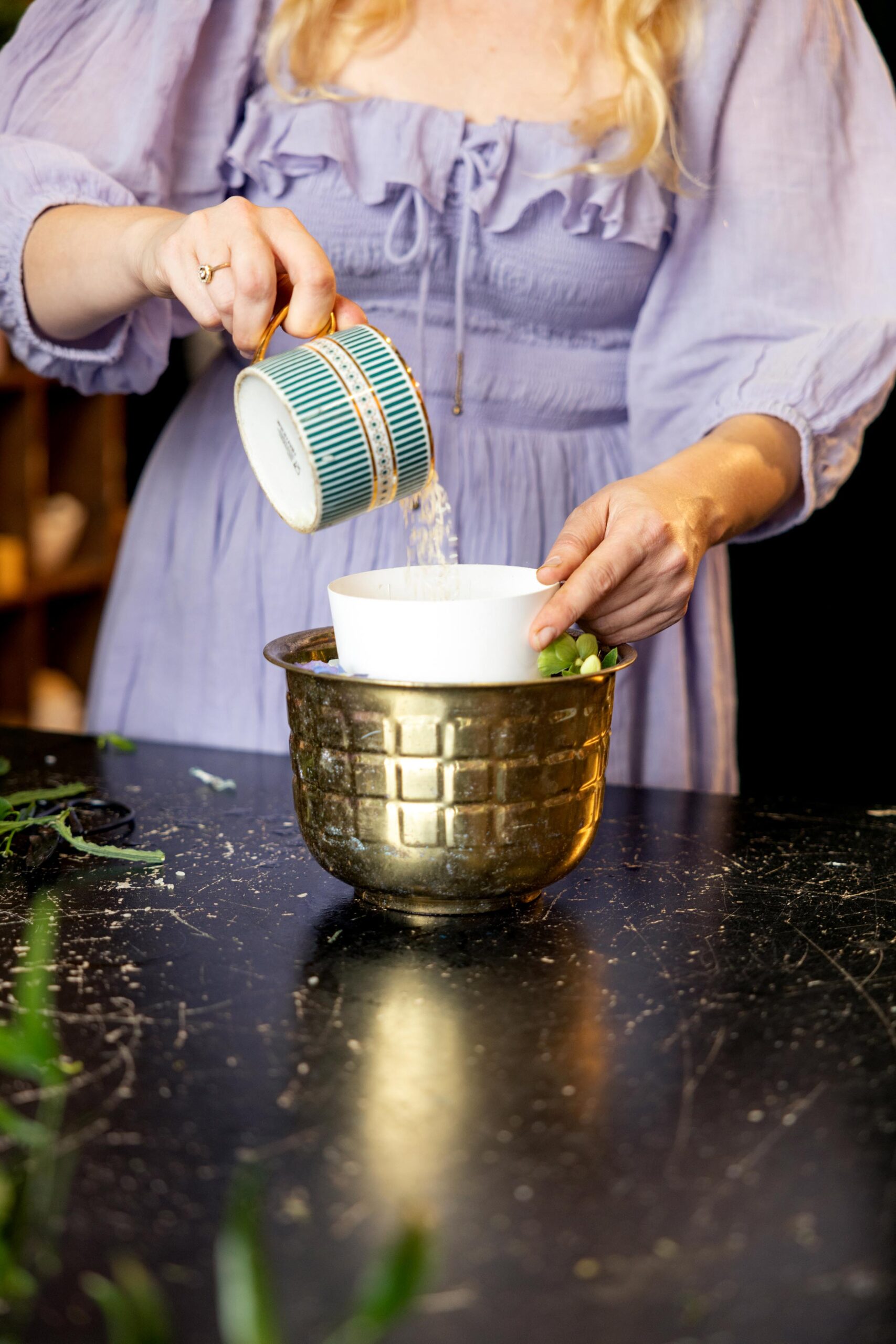 A woman in a purple dress pouring rice into a small vessel inside the medium bowl