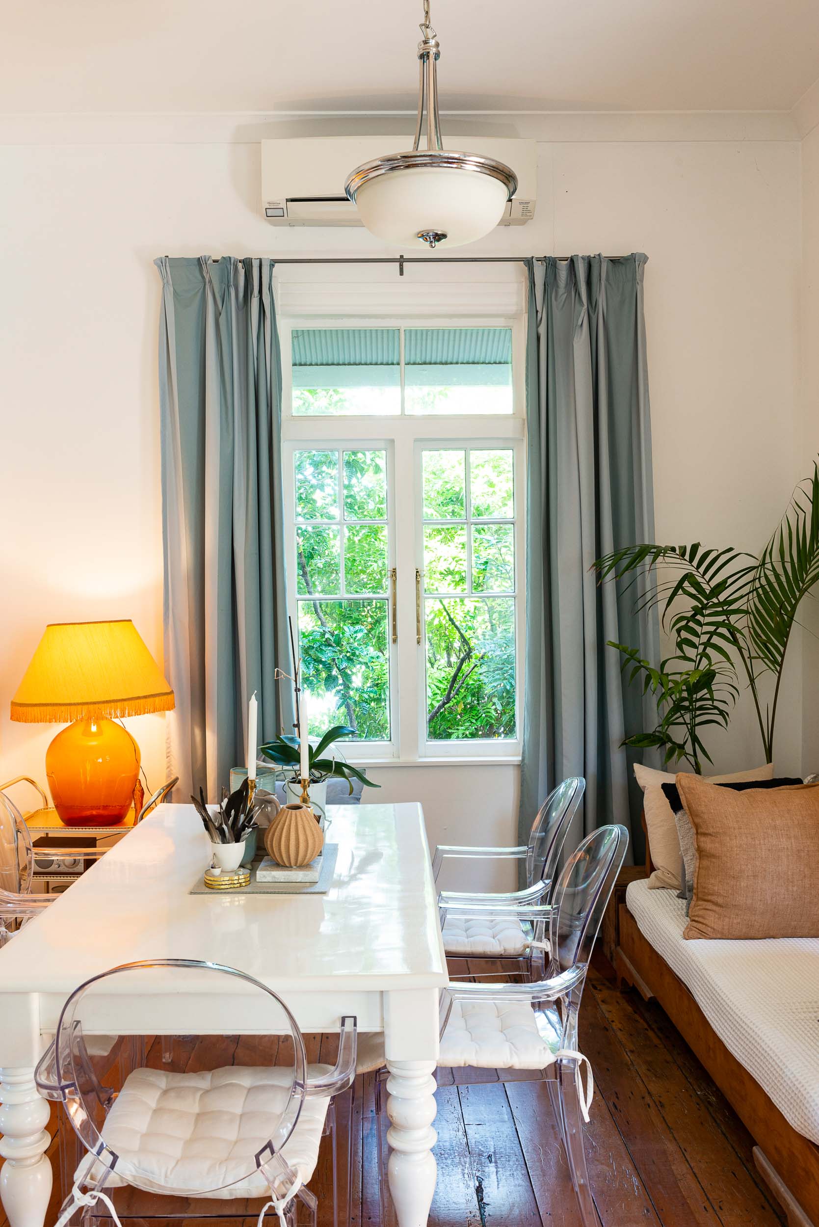 Dining room with white table and perspex chairs, a couch is to the right