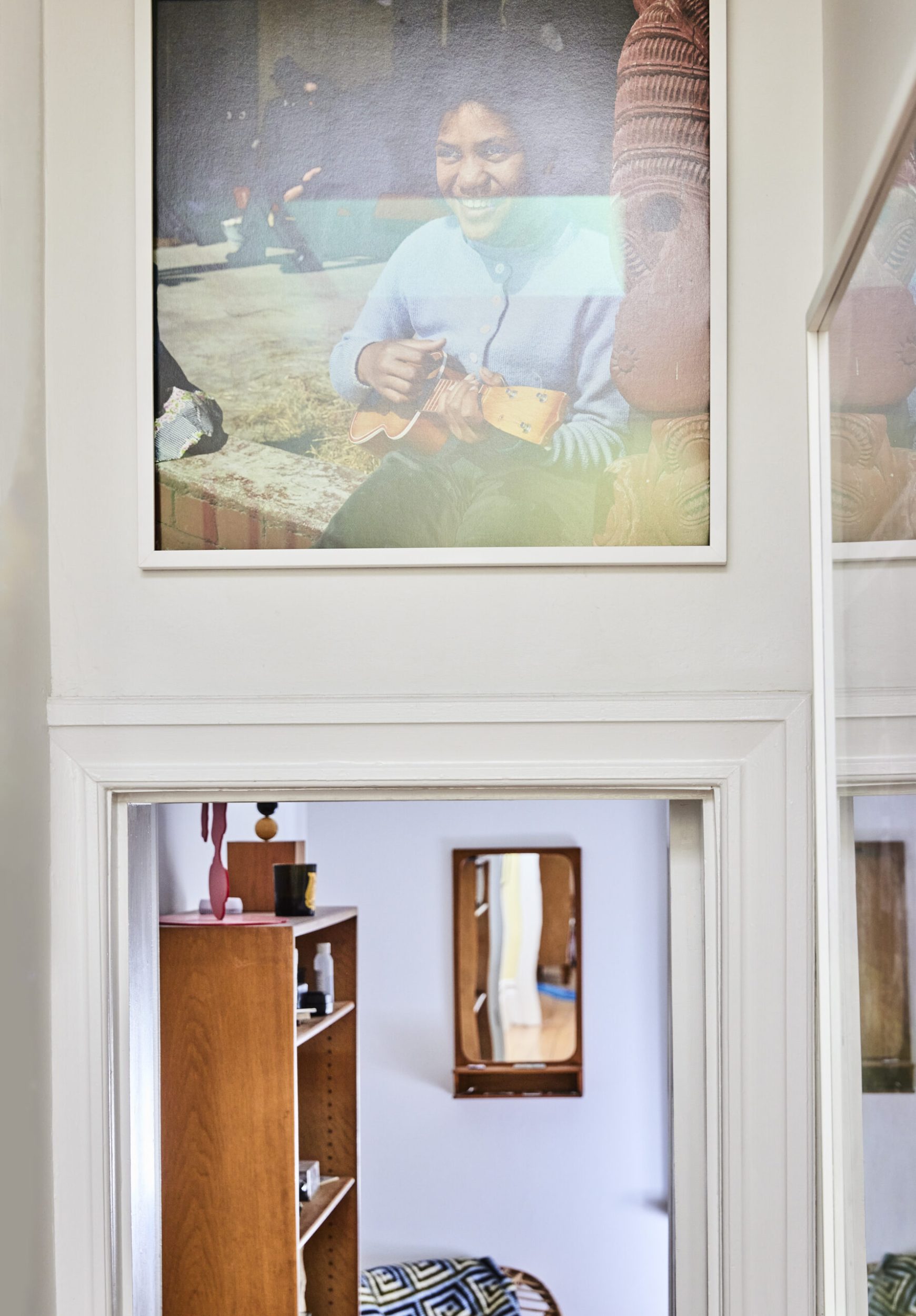 A hanging framed photograph of a girl smiling while playing guitar hanging above open door 