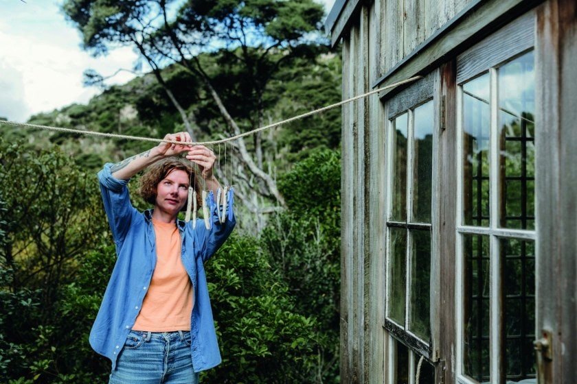 Kate Newby wearing blue top and blue jeans hanging art on a line outside her house