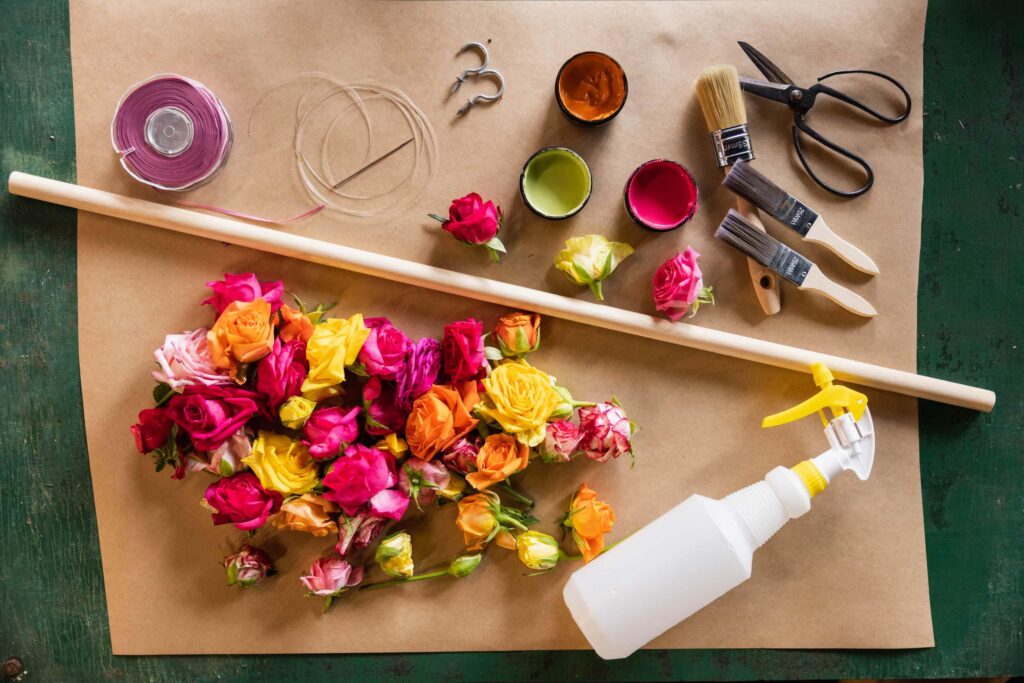 roses, dowel, wire, scissors, test paint pots, paint brushes, and a spray bottle laying on a piece of parchment paper