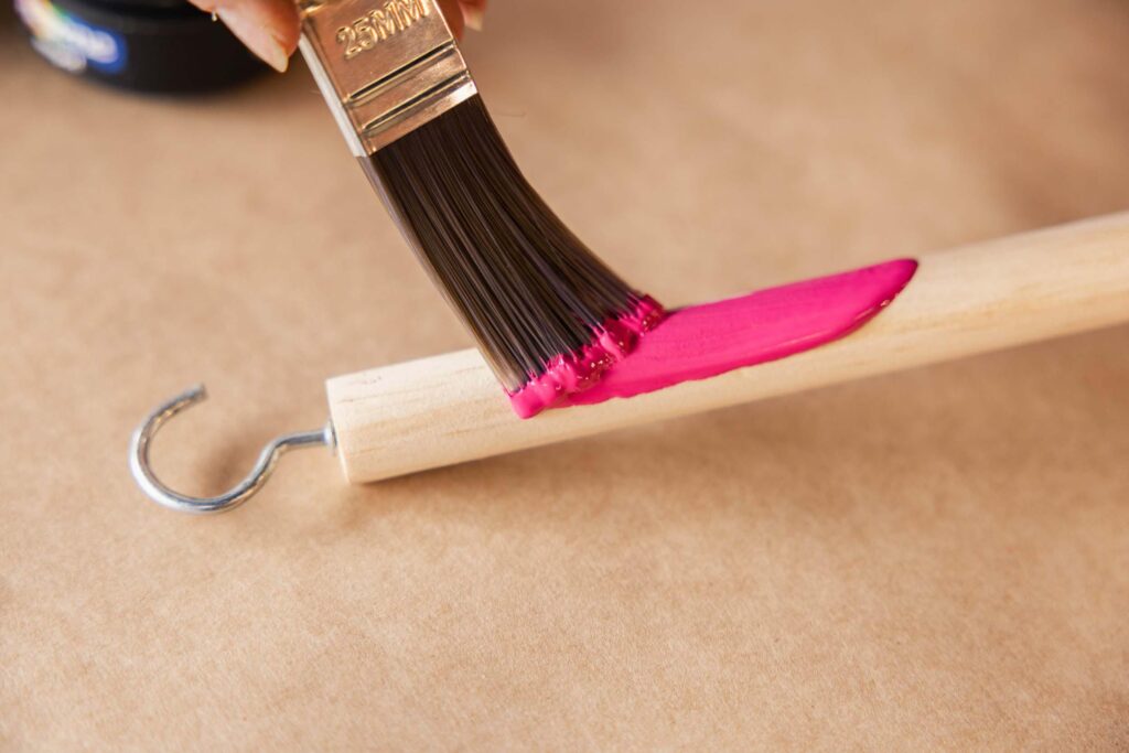 pink paint being painted onto a piece of dowel with a hook in the end