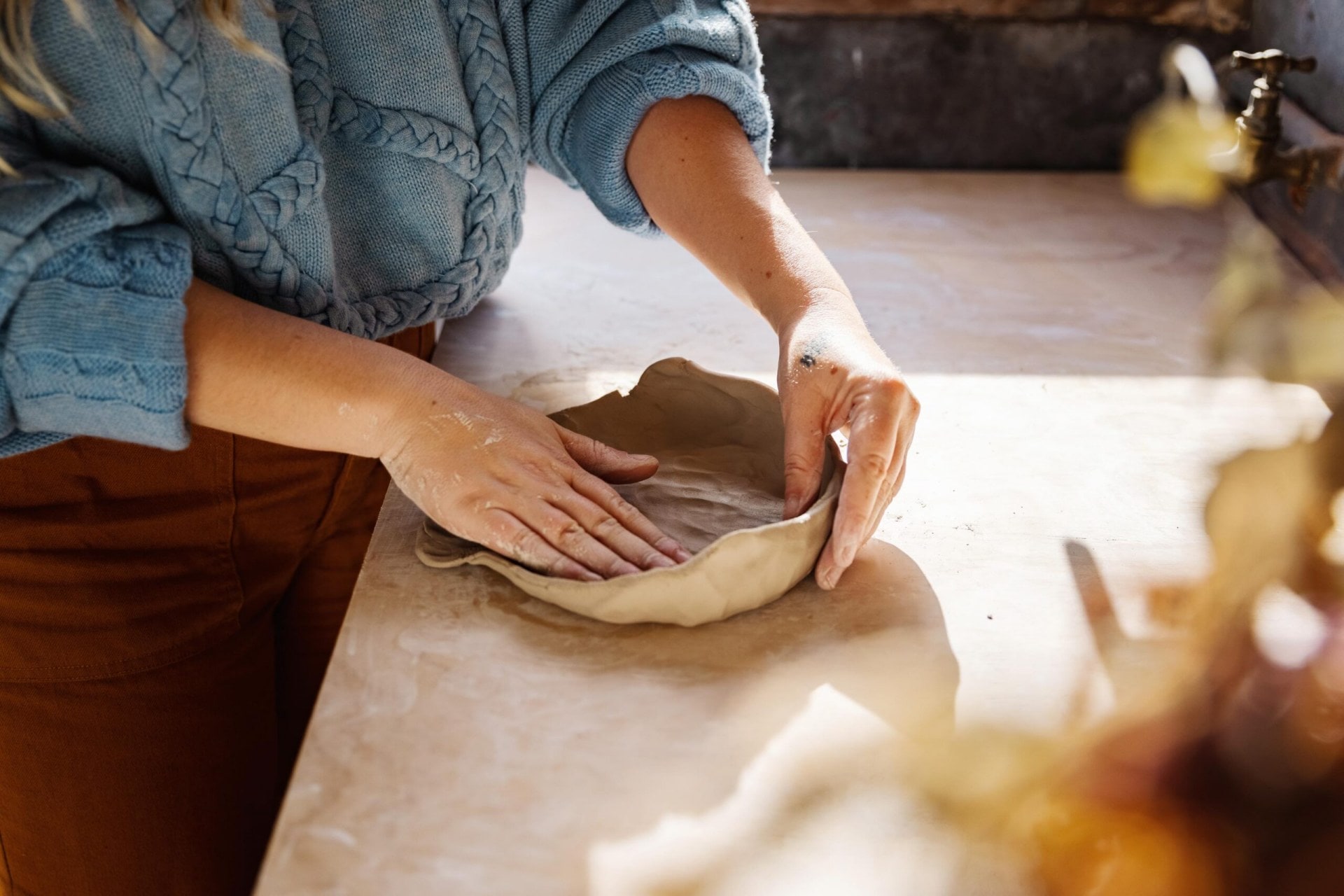 A woman moulding clay with her hands.