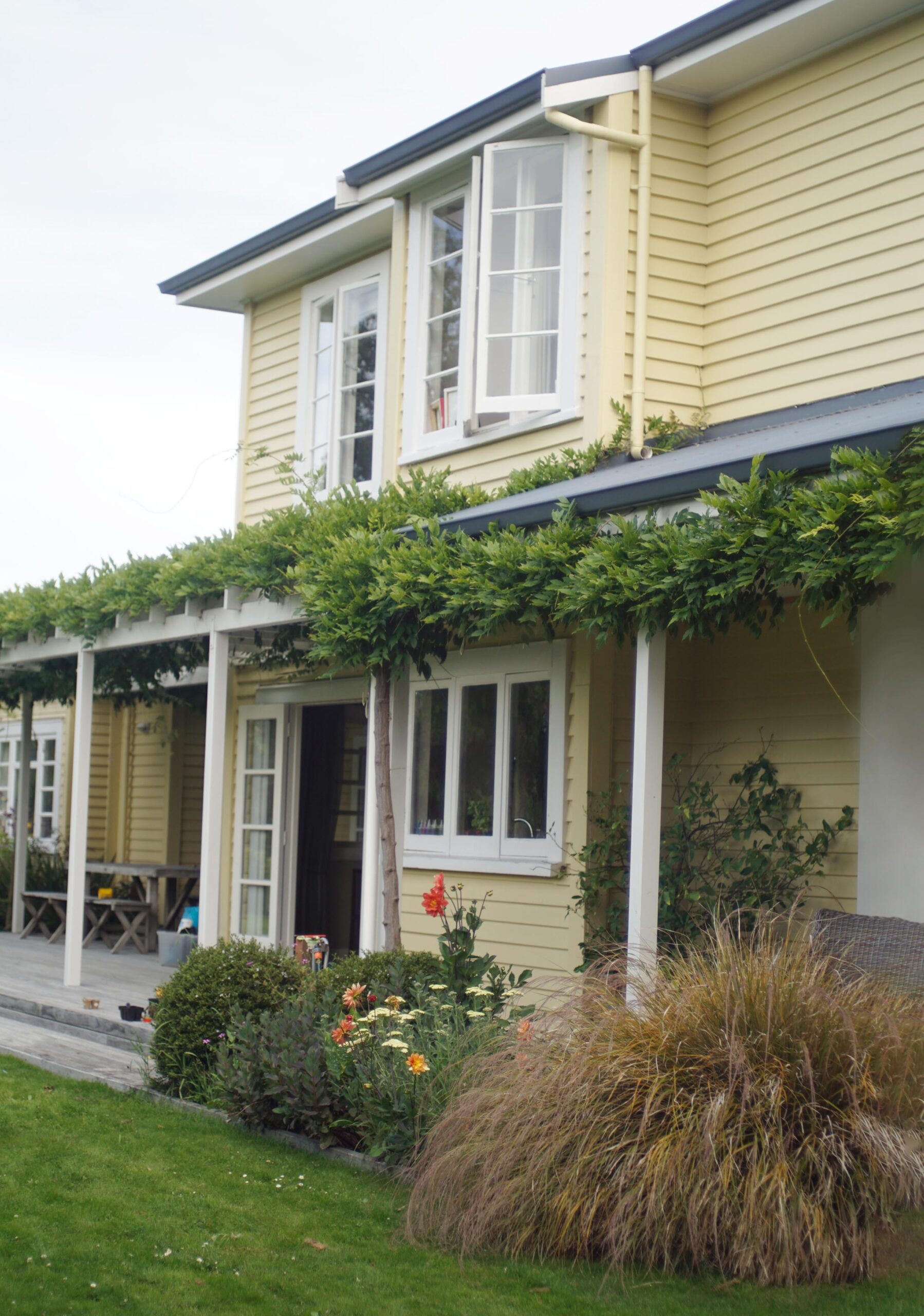 A yellow weatherboarded house covered in greenery.