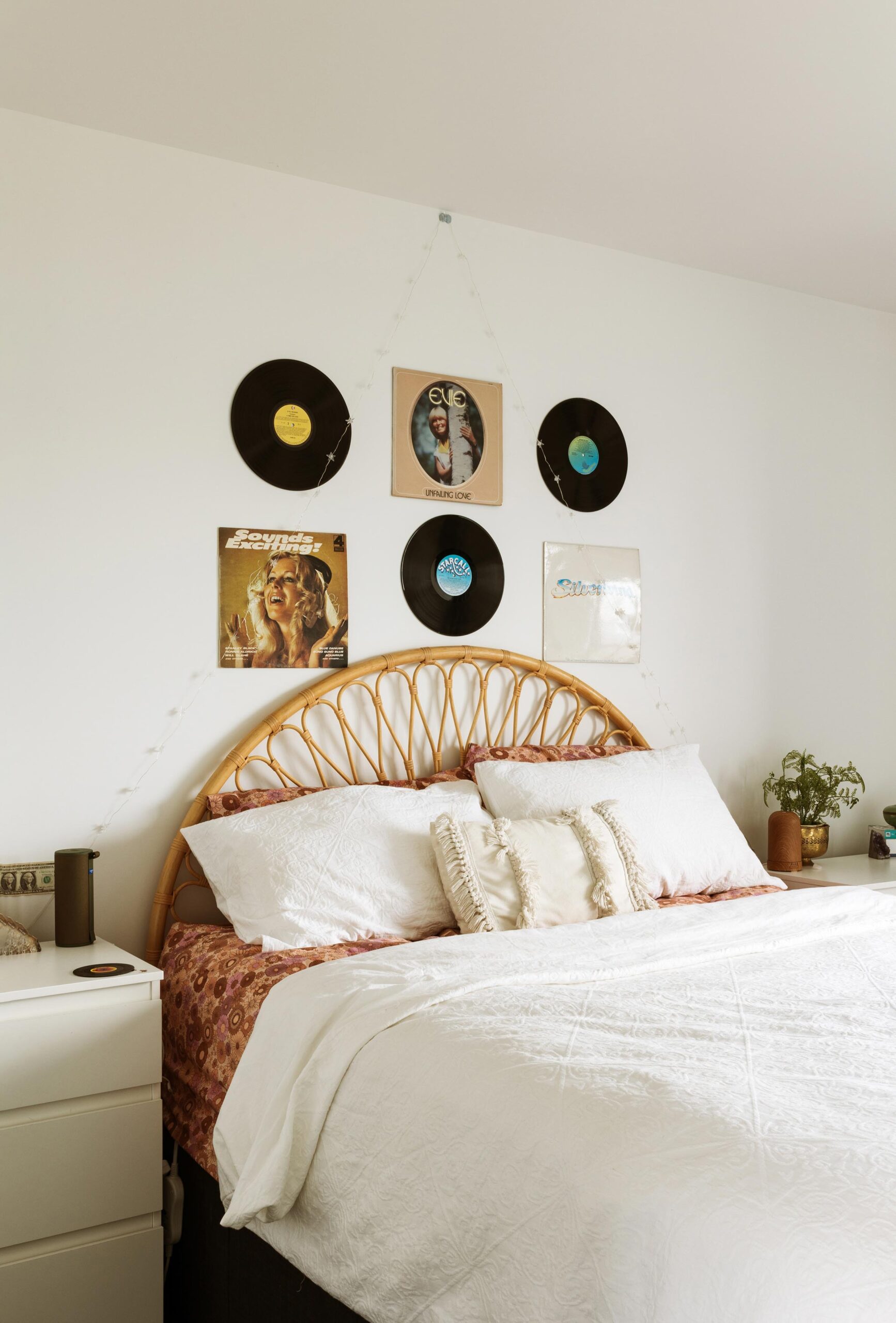 A large bed with rattan headboard and vinyl records on the wall above.