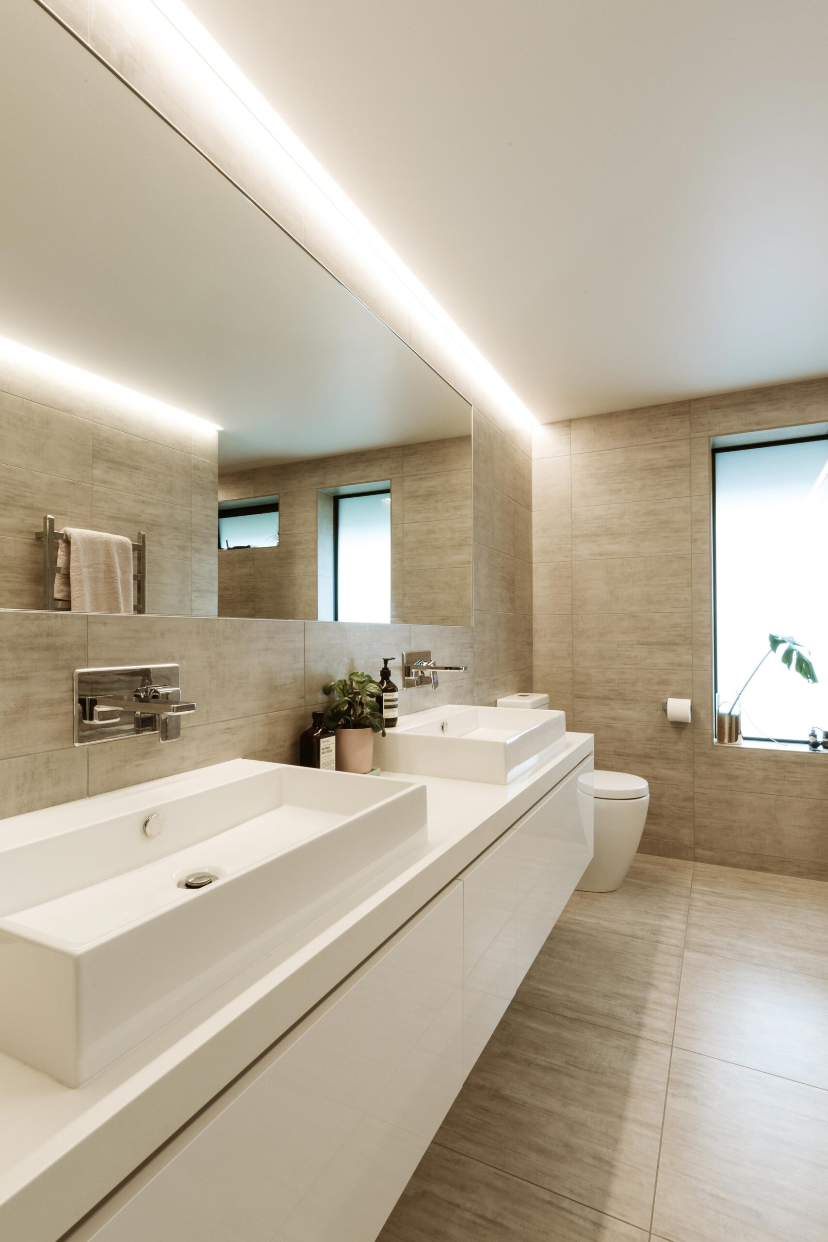 A neutral-toned bathroom with double white sinks below a mirror.