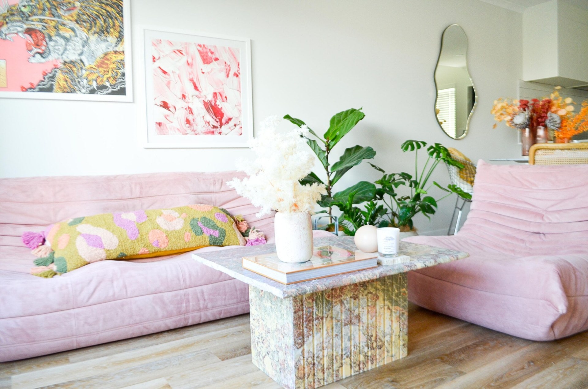 A lounge with a coffee table, a pink couch, matching chair, artwork and a mirror on the wall.