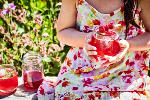 woman in white and pink dress holding a short glass with a pink liquid inside