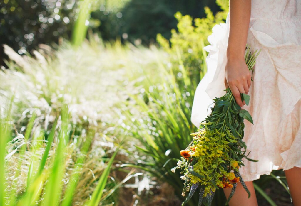 a woman holding a bouquet of wild flowers walking through a field