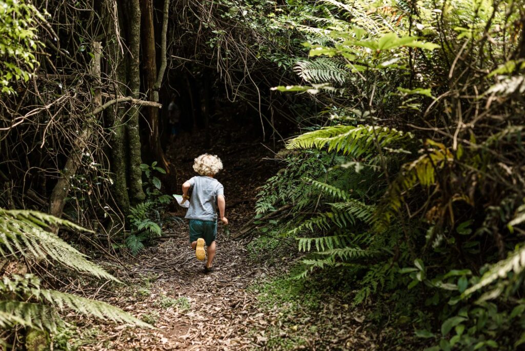 Young boy running into a lush forest