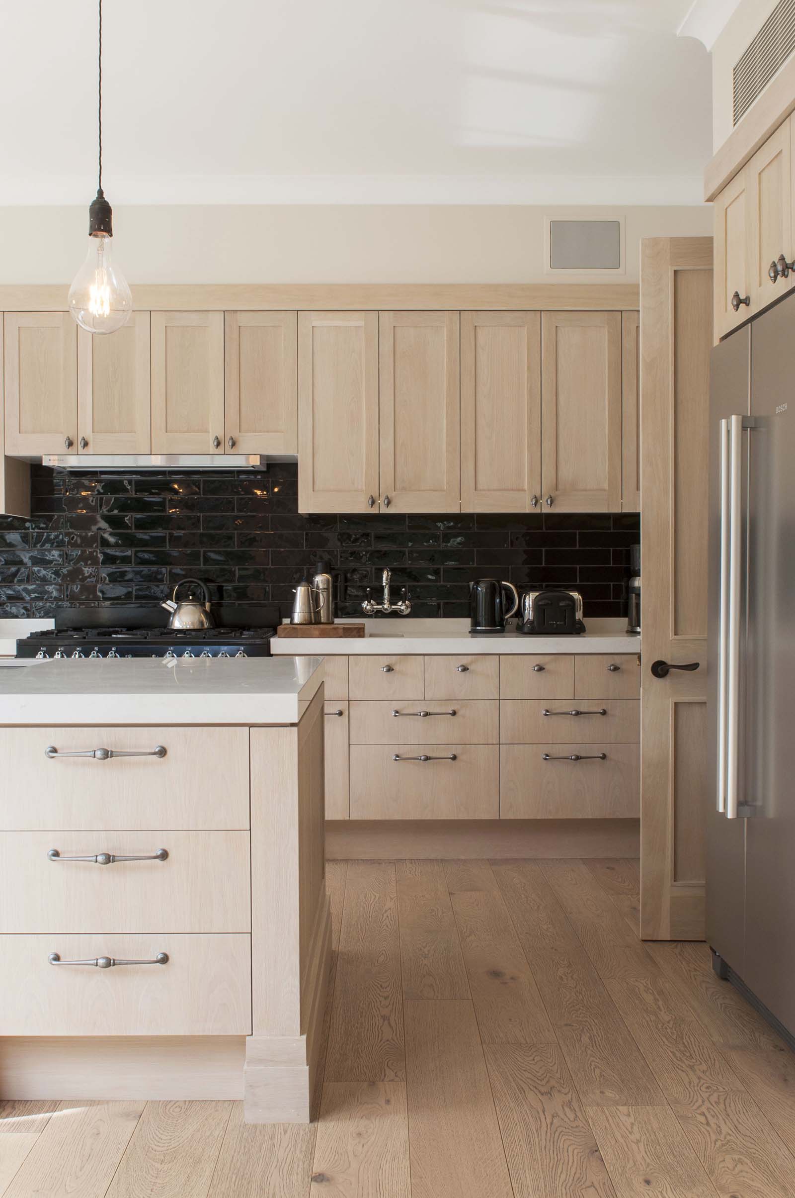 timber kitchen cabinets with black tile splashback and a timber floor