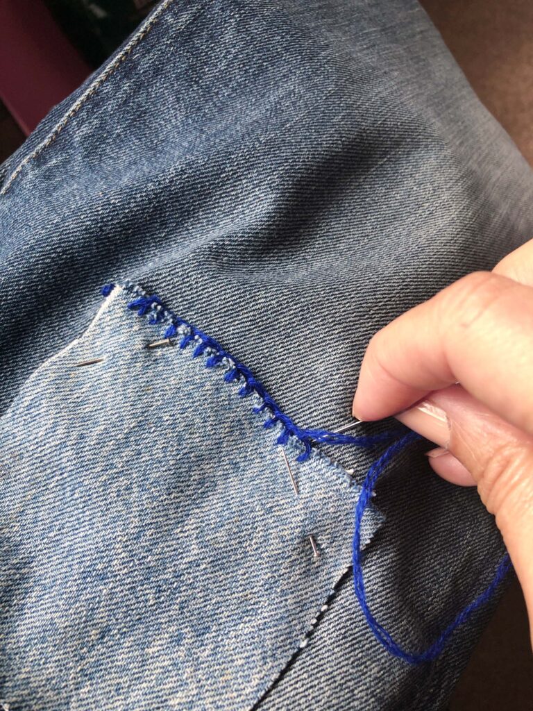 a hand stitching blue thread onto a denim pocket