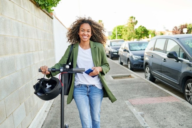 a smiling woman walking with an electric scooter